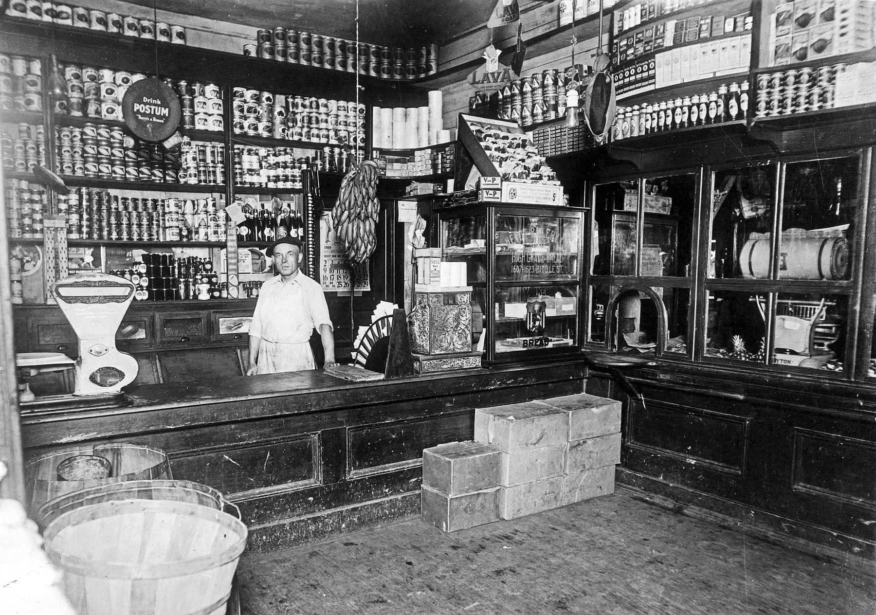 My grandparents' grocery store at 8th and Winstanley Avenue in East St. Louis, Illinois.  That intersection and neighborhood is no longer on the map having been swept away by the Interstate highway. An unnamed employee is pictured behind the counter. The store has been rearranged since the 1914 picture seen here and now has a bunch of "fresh" bananas hanging from a hook. There are no notations on the back side of the 5" X 7" print. Short sleeves and the brown spotted bananas would suggest warm weather. View full size.