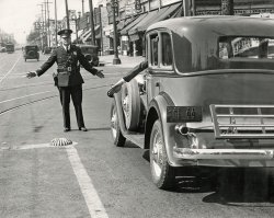 Los Angeles traffic cop/actor/chef Tom Jensen again, in the second photo of this exciting series, scanned by Shorpy member Cazzorla. View full size.
SnippetsAlthough the traffic cop is the same, along with the identical DeVaux automobile, the location is now at West 24th Street and South Vermont Avenue.
The Barber Shop and Beauty Shop sign at the upper right shows the address of the business run by Frank A. (1890 - 1950) and Gladys Whitaker at 2322 S. Vermont Avenue.
Norman deVaux, one of the DeVaux company founders, was friends with Governor James Rolph of California.  The governor sought to publicize the California motor industry.  Consequently there are several newspapers articles where the text states specifically that the governor was riding or driven in a DeVaux (which had a factory in Oakland).  
In a feature on the DeVaux Automobile in the March-April 1972 "Antique Automobile" hobby publication, Richard Larrowe stated, "Fifty new 1931 DeVaux cars that had been made specially for the factory opening, paraded through the streets of Oakland, headed by California's governor and the mayors of Oakland and San Francisco."  
Traffic ButtonCan someone explain the purpose of that traffic button on the pavement? I find it difficult to imagine its function. Thanks for any information.
[Check out the other photo linked in the caption. -tterrace]
Re:  Google Street View TodayGoogle Street View today.
Meaning of Letters on License PlatesHealdsburg Tribune, Number 92, 20 February 1932:
What the letters mean on California motor vehicle licenses plates is a frequent question among motorists, observes the California State Automobile association, which gives the following explanation of the letter system.
 ....
Automobile dealers’ cars, of course, are easily recognized by the letters “DLR” on the license plates.
(ShorpyBlog, Member Gallery)