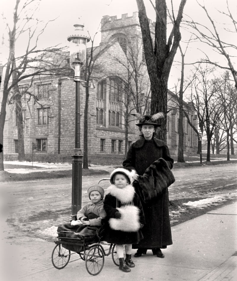 Hedwig Happel out for winter walk with daughter Johanna and son Hermann (in stroller) in Buffalo, N.Y., c. 1915.

Their attire seems rather upscale. The family was never wealthy, but mechanical engineers at that time were in demand and paid well (similar to physicians today).  One stroller wheel appears to have a chip out of the rubber.

My online research leads me to believe that the building in the background is the Central Presbyterian Church.  The church building was constructed in 1910 and sits at the corner of Main Street and Jewett Parkway. 

[Edit 12/10 - Looking at Google maps I realized that I uploaded the image reversed.  I flipped the image and re-uploaded it.  The correct orientation has the stroller on the left side of the image.]

[I've corrected it now. - tterrace]
View full size.