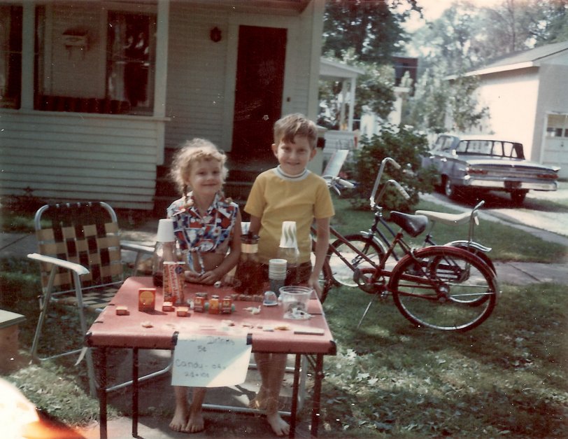My brother Patrick and I selling odds and ends at our lemonade stand in Potsdam, NY, though I think it was actually Kool-Aid. My parent's 1964 Mercury Monterey is parked in the driveway. It had a power back window (not just side windows). Some kid came by to buy our stuff who had a banana seat on her bike. I got one later on. We spent all summer barefoot. View full size.
