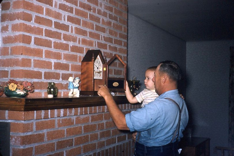 This was on my Granddad's farm, near Blandinsville, Illinois, in 1954. He is showing me the interior of his clock, how the pendulum swings back and forth and where the chime hammer falls. The winding key is in the face and it is a little after 10am. I was never a night person. The clock now sits on my parent's TV stand and it will come to my house some day. I will have to find a special place for it. View full size.
