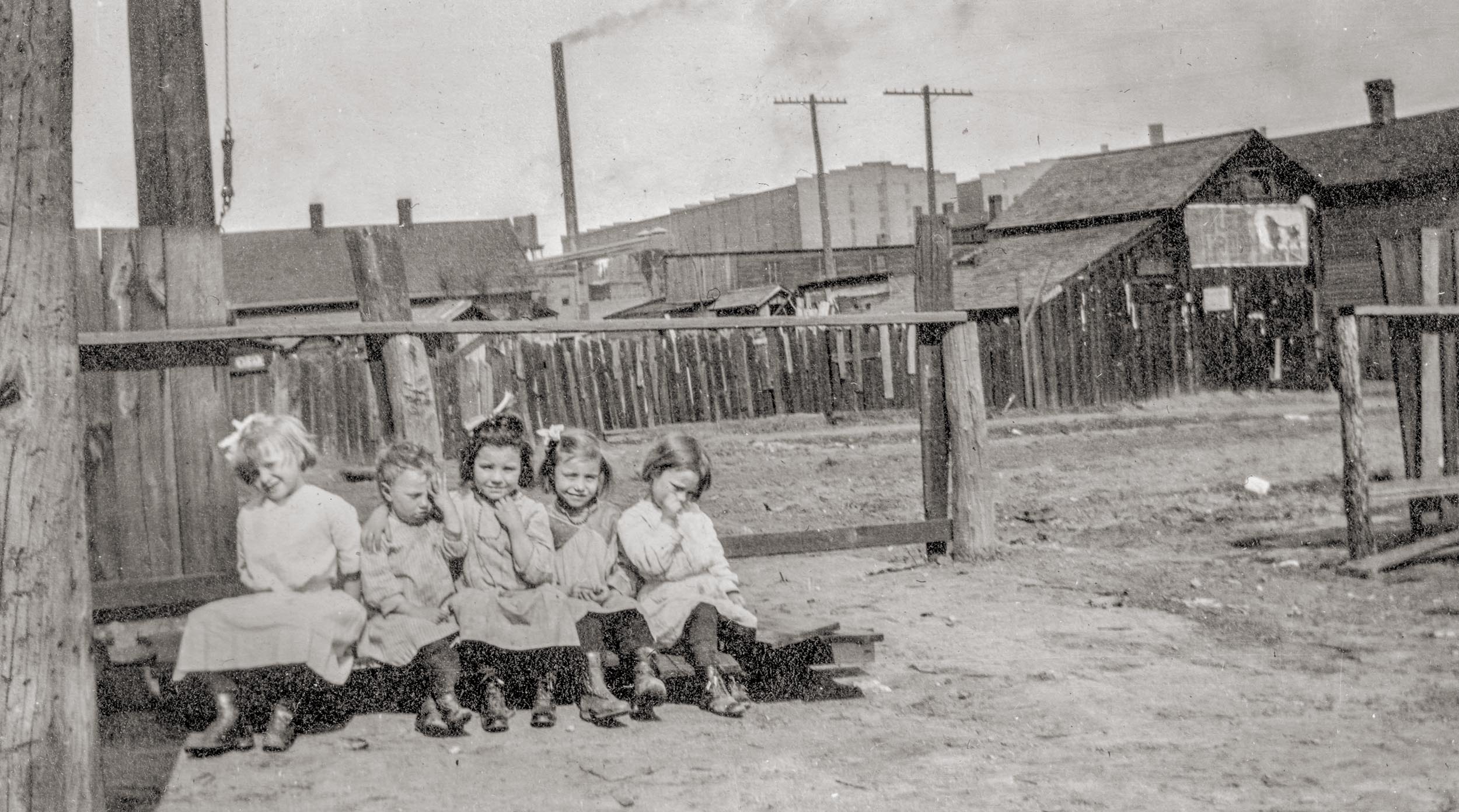 A group of girls posing for a photo, before being transported to a dinner meal at the Peoria, Illinois, Neighborhood House, which delivered meals to the elderly and fed children in a cafeteria.

The girls lived in the slums at Cinder Point between the Railroad and Illinois River, at the foot of Sanger Street, nearby the Flatboat City locale, Peoria, Illinois, circa mid-1930s. The Hiram Walker & Sons Distillery plant can be seen in the background. Picture taken by an unknown employee of the Neighborhood House.