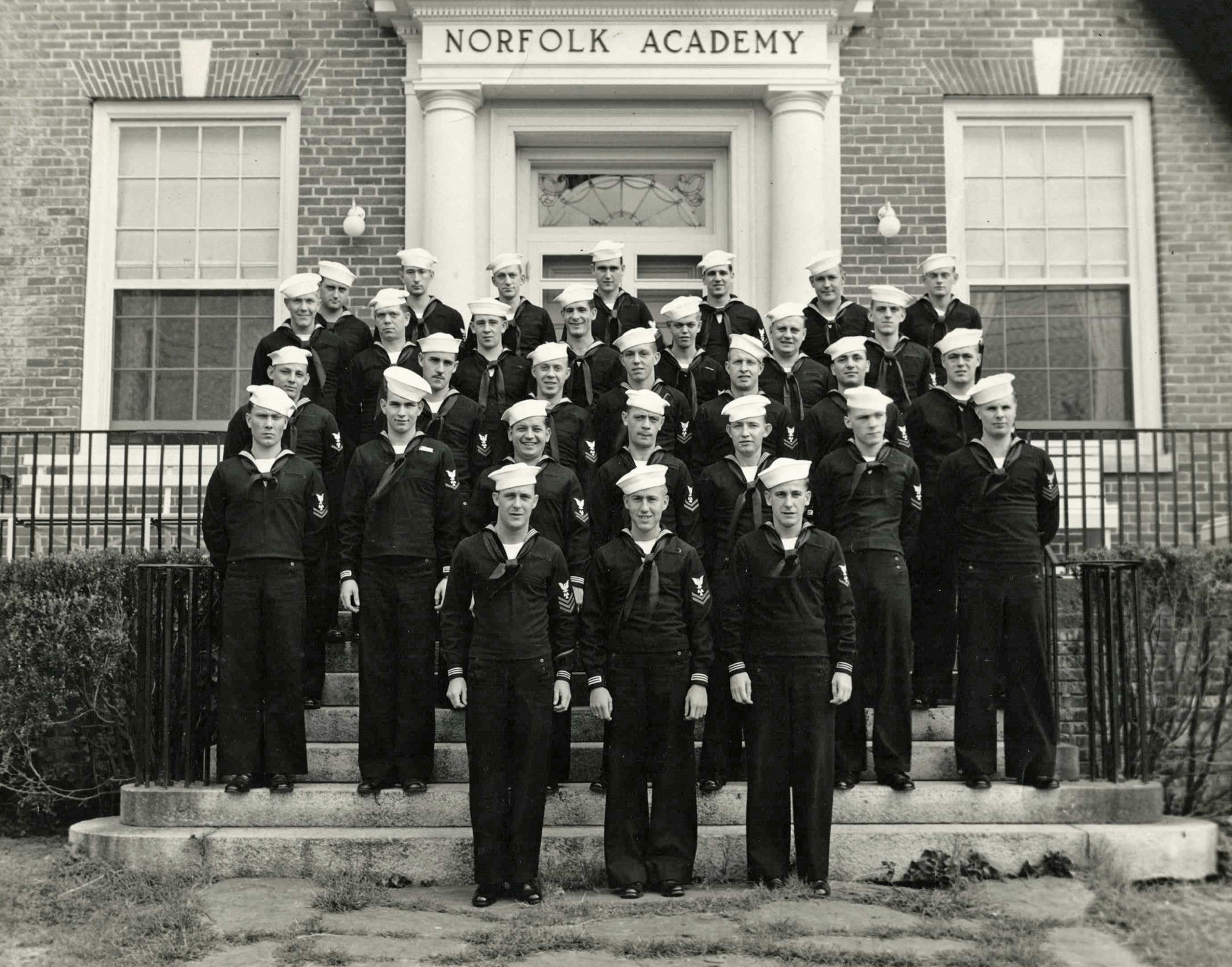 Another photo from the Navy career of James Thurston Watson (2nd row from top, 4th swabbie from left). Seems to be a machinist mate school held at the civilian Norfolk Academy in Hampton Roads, Virginia. Their names and home addresses are written on the reverse of the photo and this group was from every corner of the US. 

He joined the USS Anne Arundel AP-76 (commissioned September 1942) and sailed for the November invasion of North Africa. Called Thurston by his family, he became one of the chief petty officers of AP-76 and remained aboard until joining another ship at the end of the war. In addition to North Africa, Thurston was a veteran of Stuka attacks off Sicily, the North Atlantic convoys, the Normandy invasion, and Kamikazi attacks at Okinawa. Ten days after the surrender Anne Arundel steamed into Tokyo Bay. View full size.