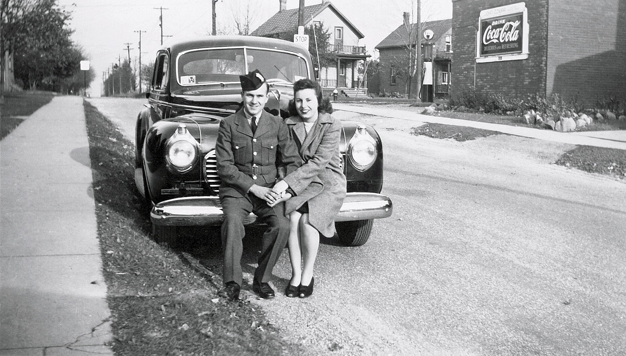 Photo of Frank Modrowski and fiancee Jen Reidel on a 1941 Plymouth Deluxe. The photo was taken in Kitchener, Ontario during the summer of 1941 while Frank was on leave with the Canadian Army. 

The photo was taken by a family member with a 35 mm camera. Frank tells me that the Plymouth was his father's, and the photo was taken in front of his parent's house. He also says that the Plymouth was a dark blue, and his uniform was a light tan -- standard summer issue for a Canadian private.

In the background is a one-pump Esso service station where gasoline was sold at 14 cents a gallon. The Coca-Cola sign displays the name of the service station owner; John Dziura. View full size.
