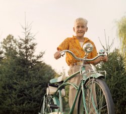 Here's a second look at my husband Peter's Rollfast Deluxe bike.  Chenango Bridge, New York, 1959.  Anscochrome slide. View full size.
That&#039;s a beauty for sureLiving in the coal mining town I grew up in in the 50's and 60's.
A bicycle that nice would get you beat up everyday. Nobody had that kind money to buy one. 
Nice shirt.Would be fashionable today, even.
Perspective of TimeI look at that bike now and think "It's cooool, maaaan."
But I know my 12-year-old 10-speed riding self would vehemently disagree. "Ugh, those handle bars.", she would say, turning up her nose.
With a Rin Tin Tin belt buckle!This young man is seriously stylin' with the new bike and the Rin Tin Tin belt buckle.  
The Folly of YouthI cringe when I think of all the bikes that I destroyed as a kid. We all thought that the fancy stuff was for sissies and girls. Fenders, racks, bells, bags, lights all went into the junk pile. All the stuff that a restorer pays a premium for today.
About the shirtI arrived on the hallowed shores of the US that same year and was about the same age as Peter.  After spending the previous 5 years going to school in a grey shirt and grey shorts, the wildly colored and paisley patterned shirts that I would now be required to wear to school pretty much freaked me out for a few months until I got used to them.
Memories!When I was 8 I wanted a bike.  I can't remember if it was for my birthday or Christmas but Dad bought me a Rollfast bike.  It was green. I must have ridden at least 100 miles on it during the next 8 years.  By the time I was 15 or 16, it definitely as NOT cool to ride a bike so it went in the garage and who knows what happened to it.  
Home SewnThere's a very good chance that Peter's mother sewed that shirt - she made most of her own clothes, including the dress she wore at our wedding.  
(ShorpyBlog, Member Gallery)