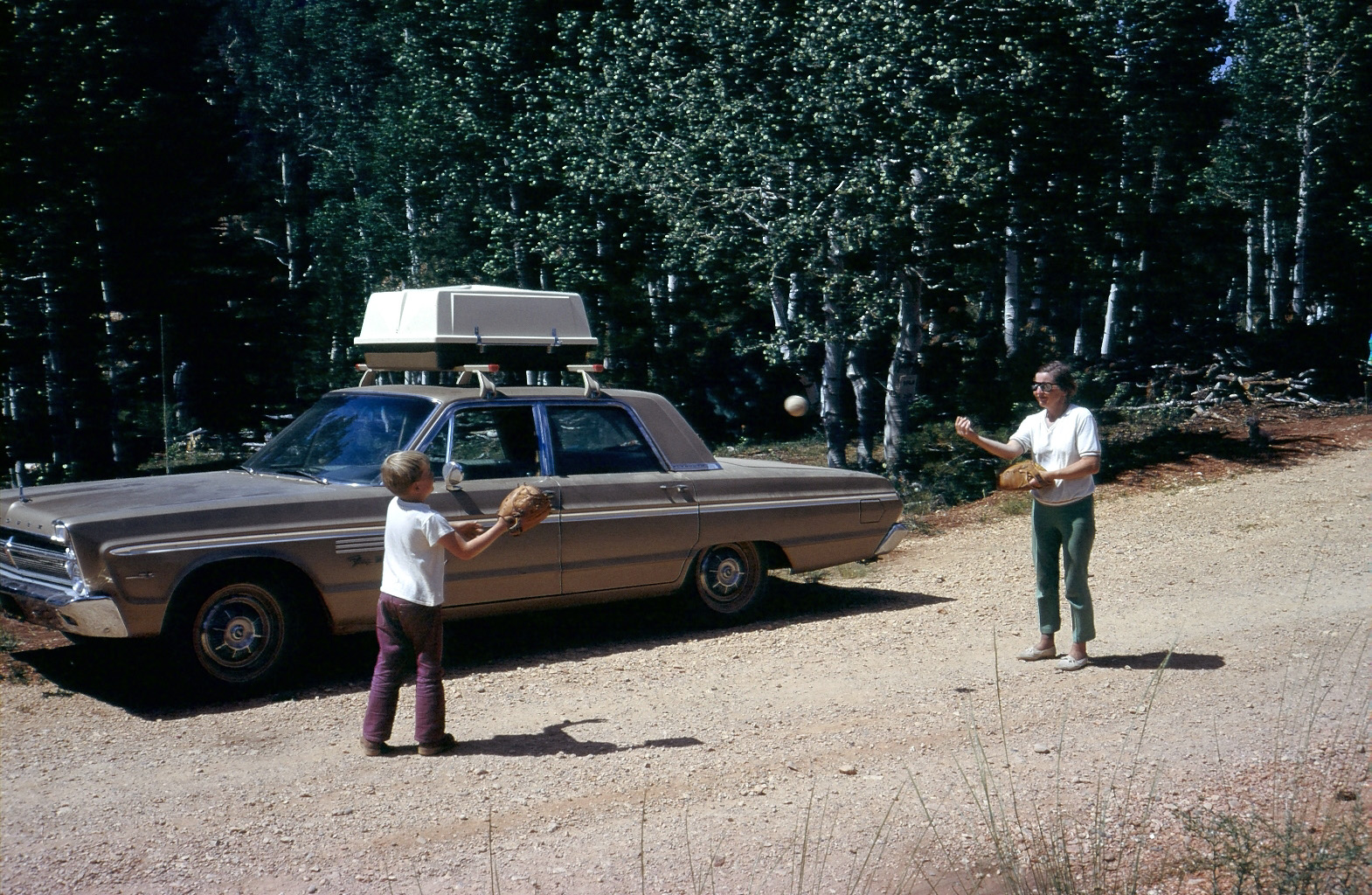My parents bought property in Southern Utah about 1970 with the intention to build a cabin for our family.They did,and it took over a decade to finish. But the work was worth it.

It was eventually sold in the early 90s to help with their retirement.

Here are my little brother and our Mom playing catch on the dirt road near where our cabin would be.

The car is our 1965 Plymouth Fury III with a massive 383 cubic inch  gas guzzling V-8, a car which would haul the trailer we stayed in up there. I drove that car as a senior in high school;it was a thrill to drive up to my friends homes with that burbling exhaust promising teenage adventure.
