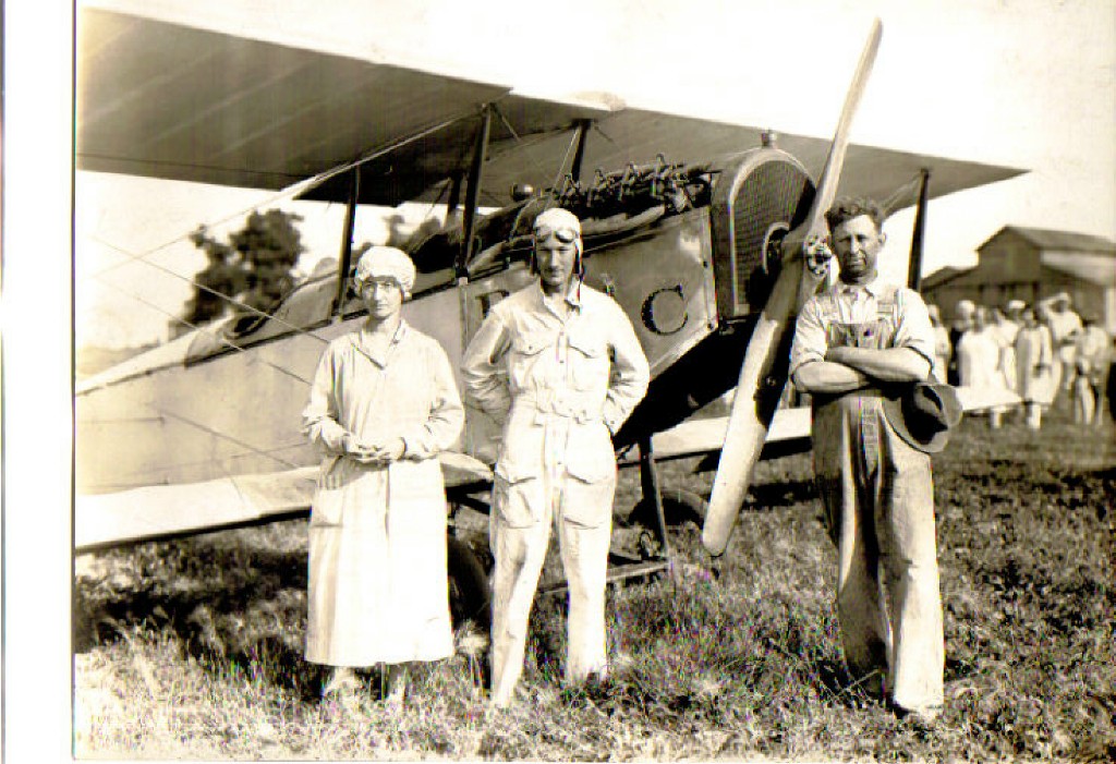 This May 1928 photo shows a young Red Irwin, standing between his parents Minnie and Wilbur, after having made the first airplane landing at Hooterville Airport. Red is wearing a white muslin flight suit and cotton flight helmet. He's flying a 1918 Curtiss JN-4 "Jenny" with an OX-5 water cooled engine. The Jenny was two place and cruised around 95-100 mph. The straight blade propeller is commonly known as a toothpick prop. 

