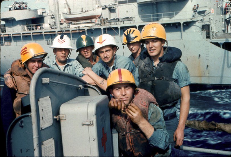 This was taken in 1960 aboard the USS Orleck just after we had finished refueling from the ship in the background. The non-regulation helmets were hand-painted by the individuals wearing them and were tolerated by the officers on board. The most appropriate is probably the one with the greasy hand as this was a messy task. Note the soiled life jackets and the hands on the sailor in the foreground. I took the picture using 35mm Kodachrome slide film. The camera was a Taron Rangefinder which was a pretty good shooter to own on a sailor's salary. 
The ship survived being scrapped and is now a museum in Lake Charles, LA. View full size.
