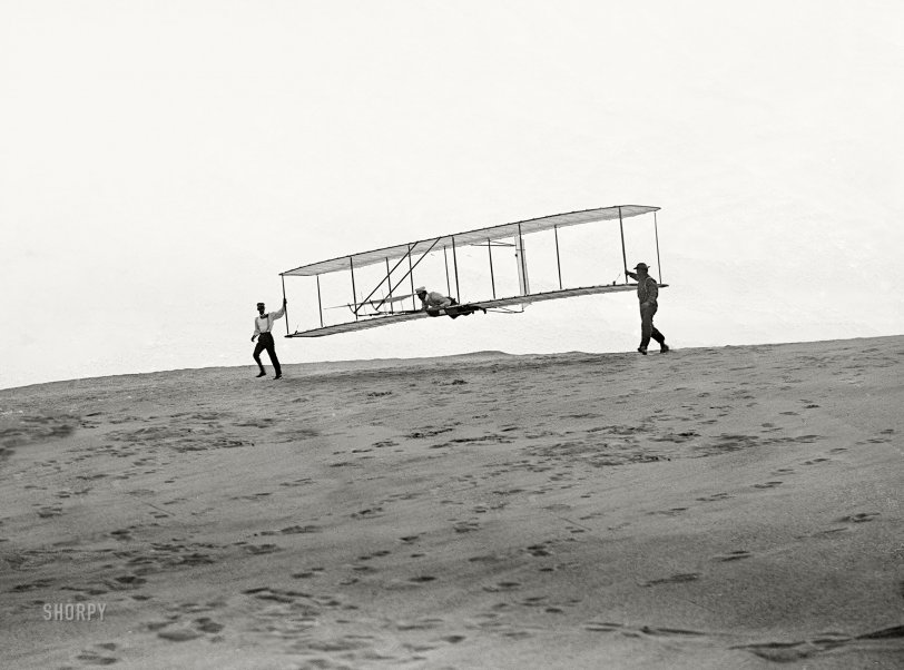 October 10, 1902. Kitty Hawk, North Carolina. "Start of a glide; Wilbur in motion at left holding one end of glider (rebuilt with single vertical rudder), Orville lying prone in machine, and Dan Tate at right." 5x7 dry-plate glass negative attributed to the Wright Brothers. View full size. This is a cleaned-up detail from the post above.
