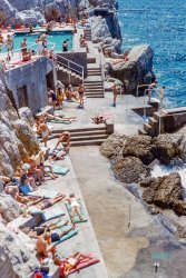 August 1954. Antibes, French Riviera. "The Sporting Look -- Beachwear. Sunbathers at the Eden Roc, Côte d'Azur." 35mm Kodachrome slide by Toni Frissell. View full size.
Sun protectionGeez -- no place to stick your umbrella in the sand.
Bond, James BondI embigulated and looked for Sean Connery everywhere but couldn’t find him.
Bird is the wordThere are a lot of budgies getting smuggled there.
Bond, James BondI think I found him.
Missh Moneypenny, let me get your legsh for you.
Are those ...... swings and rings dangling over the ocean for acrobatically getting into the water?  If so -- yeow!
It looks très really niceHere is the hotel to which the swimming pool belongs.  The pool has been enlarged and the steps reconfigured.  Too bad it was empty when the Google satellite passed over.
Click to embiggen

Bikini scarcityThe bikini, a postwar sensation of French design, is rather scarce here. I count two.
For the Rich and maybe famousThe Hotel du Cap-Eden-Roc is booked solid until October 2023. Even then, get your wallet out.
The wonder of KodachromeKodachrome, now an obsolete format, never ceases to amaze in its dazzling rendition of color. 
I have a very large collection of National Geographic Yearbooks, and one of the joys of looking through the pages is the incredible Kodachrome photographs, taken by very talented photographers.
Kodachrome can be considered the equivalent of moving pictures' Technicolor, although a different production process is used, the effects are similar.
(The Gallery, Kodachromes, Swimming, Toni Frissell)