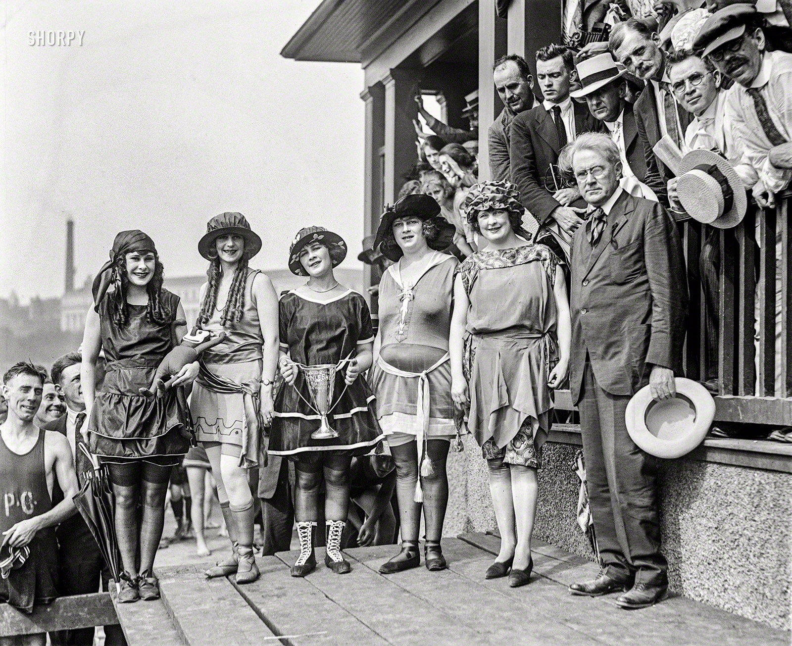 Lansburgh Girls Win Style Prize
Five Models Gain Cup at
Tidal Bathing Beach Costume Show.
&nbsp; &nbsp; &nbsp; &nbsp; With five models displaying the most modern bathing costumes, Lansburgh & Brother won the prize cup at the first annual style show, held yesterday afternoon at the Tidal bathing beach. The models who represented Lansburgh's -- all local girls -- were Mary Lee, Iola Swinnerton, Thelma Spencer, Hattie Spencer and Julia Cunningham. The suits which they wore were special importations, brought to Washington for exhibition at this show ...
 -- Washington Post, 6/26/1921

Washington, D.C., 1921. "Bathing Beach costume contest." At left we have Iola Swinnerton, First Lady of Shorpy in perpetuum; the others are plebeian ciphers spared total invisibility only by the grace of her luminous beauty. View full size.