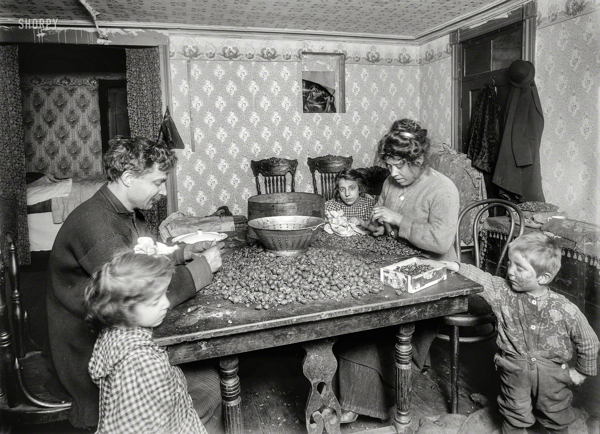 December 1911. "3:30 P.M. -- Picking nuts in dirty basement tenement, 143 Hudson Street, New York. The dirtiest imaginable children were pawing over the nuts, eating lunch on the table, etc. Mother had a cold, blew her nose frequently (without washing hands) and the dirty handkerchief reposed comfortably on the table and close to the nuts and nut meats. The father picks now -- 'No work to do at any business.' (Has a cobbler's shop in the room.) They said the children didn't pick near. (Probably a temporary respite.)" The Libertine family, seen earlier here. 5x7 inch glass negative by Lewis Wickes Hine. View full size.