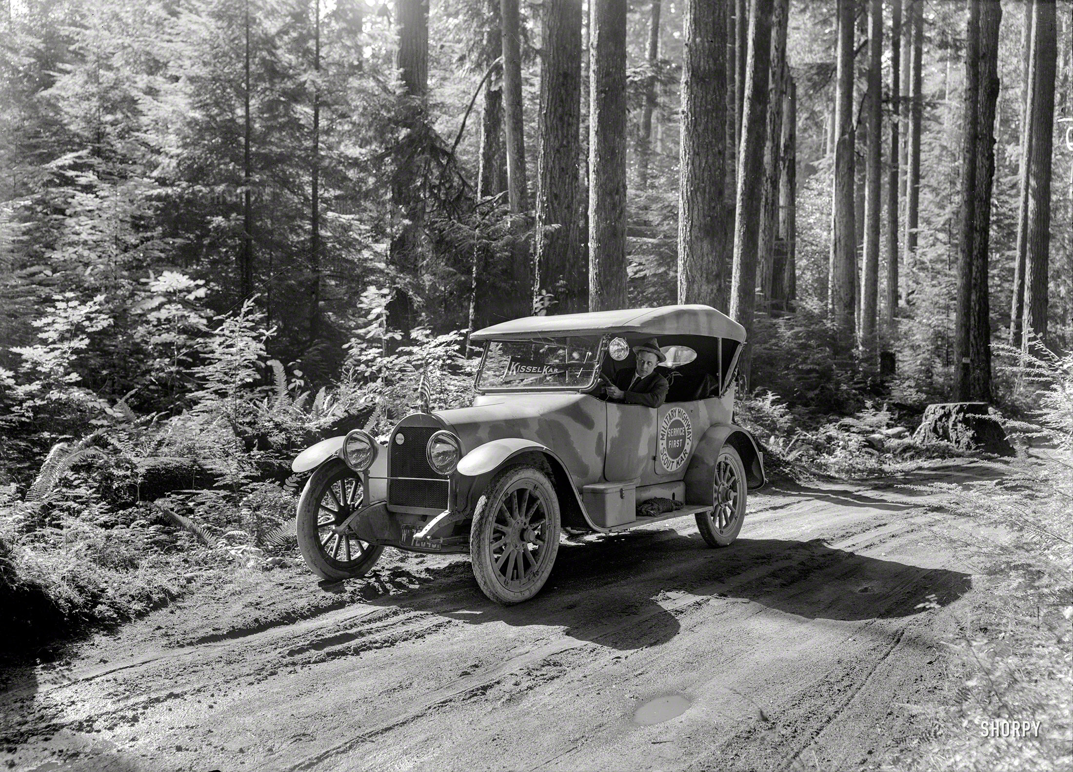 &nbsp; &nbsp; &nbsp; &nbsp; America's first camouflaged automobile has been let loose, and is now on the war path. The inhabitants of the Pacific Coast from Seattle to San Diego swear they are "seeing things." A sheriff who has a record for pinching speeders is out after the camoufleurs who committed "camouflage" to prove that America's automobiles are as chameleon-like while on the war path as those in Europe.
-- Oakland Tribune, Oct. 28, 1917

&nbsp; &nbsp; &nbsp; &nbsp; W.L. Hughson, of KisselKar fame upon the Pacific Coast, has donated the famous Kissel military scout car, recently used to blaze the "three nation run," to the government department having the new operations of "camouflage" in its charge. A committee of three prominent San Francisco artists will paint this car with color patches, which suggests nothing except the surrounding earth, trees, grain fields, sky, etc., making an exact fac-simile of the cars now being used by the allies along the various war fronts
-- Motor West, Oct. 15, 1917
"Kissel Military Highway Scout Kar." From somewhere in the woodsy Pacific Northwest comes the "Scout Kar" last seen here, with 1918 Washington State dealer plates. 5x7 glass negative by Christopher Helin. View full size.