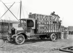San Francisco, 1920. "Diamond T truck -- DeLand &amp; Son Draymen." Draymen and drayage being haulage-related terms that eventually became as extinct as the Diamond T. 5x7 glass negative by Christopher Helin. View full size.
Without fixed sidesAnother aspect in the definition of dray is a cart without fixed sides, as illustrated in our current photo.
Drays.Dray and Draymen are still in common usage in England to describe specifically beer deliveries to pubs and bars.
But I've never heard of 'drayage' before.
Not quite dead yet"Drayage" survives! At least in exhibition halls and trade show venues, where the cost of having forty packing crates conveyed from a loading dock to a trade show booth site might just eclipse the value of the display materials themselves. In modern times, the term "drayage" connotes a mashup of operational logistics, fork lifts, and an occupational fervor reminiscent of medieval guilds. It's nice to remember the word, but you'd really better remember to allocate a big pile of cash for drayage.
TeamsterDraymen maybe extinct, but the term teamster is alive even though teams of horses were on there way out in 1920. In horse drawn parlance a dray had the rear wheels no higher than the deck of the body; a wagon with rear wheels that extended above the deck was called a truck.(simplified explanation)
DrayageDrayage as a term is not extinct yet! Here in SC, we have Smith Dray Line http://www.smithdray.com/ . Moving and storing since 1888! Not that anyone would ever suggest SC is mired in the past or anything....
Last MileGranted, the term may be extinct, but draymen and drayage are here to stay. Drayage hauling is one of the most critical components of the global economy's intermodal transportation system. Goods crisscross the globe by rail and ocean freight faster and cheaper per ton than ever before, but still must get from the rail yard or port to customers. This "last mile" of delivery is still done by truck, though Diamond Ts are hard to find. 
All of those brown trucks and red-white-blue trucks delivering Amazon, Zappos, and  sexynighties.com packages are draymen. The packages arrive by air and make their "last mile" in an panel truck operated by an independent contractor, though the transportation unions would prefer employment. Check out www.drayage.com
My great-great grandfather ran a drayage company by covered wagon from the rail yards to rural customers in Comanche County, TX. He died of pneumonia in his wagon on the banks of the Brazos River in the rain waiting for the flooding river to subside so he could ford it.
More Inventions NeededSomeone needs to invent a forklift. Those crates look very heavy even if they were empty. This truck has solid rubber tires. The cargo and driver have to endure a bone shattering ride.
UK ExtinctionBritish English near equivalents for extinction are 'carrier', 'carter' &amp; 'haulier'.
Drayage Historical Turning PointDrayage got a lot easier when they started using wheels.  That didn't affect the term, however.
[A dray is a cart or wagon, so presumably they've always had wheels. - Dave]
I knew a Drayman onceAs a youth in England growing up in the East, my father ran an old sea coast hotel in King's Lynn (Norfolk) for one of the breweries.
When the men delivered the beer barrels and such, my dad referred to them as Draymen. That was back in the early 70's.
Dray definitionAccording to the Oxford English Dictionary a dray was originally a sled and later the term became applied to the low heavy wagons with wheels particularly used by brewers.
The lap of luxuryRoof, tilting "wiggly" glass windshield, padded seat &amp; backrest, leaf springs with maybe a half inch of travel.  The life of the drayman.
(The Gallery, Cars, Trucks, Buses, Chris Helin, San Francisco)