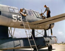 August 1942. "Aviation cadets in training at Corpus Christi, Texas, Naval Air Base." Kodachrome by Howard Hollem, Office of War Information. View full size.
KingfisherVought OS2-U Kingfisher. Instructor pilot is in the rear gunner's station. These planes usually flew off cruisers and battleships and were launched by catapult.
Let&#039;s see how longit takes to identify this unique amphibian, probably not very long.
More about the OS2Usee the site:
http://www.navsource.org/archives/01/57k1.htm
Maybe the "Jeep" of the WWII aircraft?
The Curtiss (AV-4)The Kingfisher was used extensively on Seaplane Tenders such as my father's ship, the USS CURTISS (AV-4). The Curtiss held two of these float planes in a hanger. The planes were set into the water using one of the Curtiss' huge cranes which were also used to raise and lower anything from supplies to PBY's for servicing, fueling and to retrieve film from the PBY's after they overflew islands. My father's ship had admirals quarters aboard and saw the likes of "Bull" Halsey, Chester Nimitz, Secretary of the Navy William Knox and Lt. Col. Evans Carlson legendary leader of "Carlson's Raiders" of the USMC. The Curtiss served as flagship for Commander, Naval Air, South Pacific.
The Curtiss received seven battle stars for service in the Pacific theater starting with the attack on Pearl Harbor where she was damaged and including Tarawa, Kwajalein, Eniwetok, Saipan, Guam and Okinawa where she was hit by a Kamikaze killing many men. My father was one of the "Plank Owners" or part of the first crew on the Curtiss when it was commissioned out of Philadelphia shipyards in 1940.  
A floatplaneIn shipboard operations it landed on the water and was winched aboard. The wheels we see are beaching gear, attached in the water so the machine can be brought ashore and removed, also in the water, prior to a water takeoff. There was a landplane version without the float.
That photo has powerThat's a fantastically done photo. I can smell the slighty funky smell coming off the sodden, wilting Gulf breeze (what there is of it). Smell and feel the heat on that duralim skin, spiced with the trio of lube oil, sweat and sickly 180 octane av-gas. The impatience of these three as they endure the photog setting up the shot instead of being up in the cooler skies. The paint,even then,looks baked and finger smeared, reminiscent of beaters drove too long without a wash 'n' wax.
Damn fine work.  
(The Gallery, Kodachromes, Aviation, Howard Hollem, WW2)