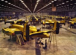 &nbsp; &nbsp; &nbsp; &nbsp; Time flies like B-25's. Another Kodachrome from the Early Days of Shorpy, enlarged and re-restored.
October 1942. "B-25 bomber assembly hall, North American Aviation, Kansas City." Kodachrome transparency by Alfred Palmer for the OWI. View full size.
I never realized how small aI never realized how small a B-25 was. That thing's tiny.
Also, where are all the people? 
Bright yellow!Not exactly a stealth bomber, eh?
Where are all the peopleMight be that a security guard on night duty took the picture.
Where the people areThey are mostly hidden by the planes. I see at least 19 people. The photographer was Alfred Palmer, who took hundreds of pictures like this for the Office of War Information.
BombersNot many of you know about WW II planes, first the rest of the outboard wings haven't bee assembled and put on yet, next the yellow color is the primer paint, the finished coat would be olive drab, camouflage or desert colors light &amp; dark sand depending what theater of war the plane would be sent to.
North American AviationThat was not a B25 (a  four engine heavy bomber) The plane in the photo appears to be the twin engined B26, a much faster, lighter "attack bomber" for lower level pin-point missions rather than the carpet bombing that actually the larger B-17's and B25's were best suited for.
B25 bomberThe B25 was a twin-engine medium bomber. I have some more pictures of the assembly line to post later in the week.
B25 bomberGood plane; wasn't it a B-25 that hit the Empire State building late in the war years??
Harry
B25 BomberYes, that was a B25. From Wikipedia:
At 9:49 a.m. on Saturday July 28, 1945, a B-25 Mitchell bomber flying in a thick fog accidentally crashed into the north side of the Empire State Building between the 79th and 80th floors, where the offices of the National Catholic Welfare Council were located. One engine shot through the side opposite the impact and another plummeted down an elevator shaft. The fire was extinguished in 40 minutes. Fourteen people were killed. Elevator operator Betty Lou Oliver survived a plunge of 75 stories inside an elevator, which still stands as the Guinness World Record for the longest survived elevator fall. Despite the damage and loss of life, the building was open for business on many floors on the following Monday.
B-25 or B24?You're thinking of the B-24 4 engine "Liberator" bomber which was cousin to the B-17 "Flying Fortress" that did carpet bombing before the advent of the B-29 "Super Fortress".  The B-26 was a twin engine light bomber made by Martin Aircraft Co, and in the same category with the B-25 "Mitchell".
This is definitely a pictureThis is definitely a picture of a B-25, also known as a Billy Mitchell.  I flew as a passenger in one of them in 1948 on my way to an Air Force tech school to become a radio operator. It had to be the noisiest ride ever in a medium bomber, but it was fast.
Kodachrome?Was this taken on Kodachrome? Look at how well the colors are retained. - Nick
[Yes,a 4x5 Kodachrome transparency. - Dave]
This is definitely a B-25This is definitely a B-25 Mitchell, not a B-24 Liberator, and not a B-26 Marauder.  I have shot B-25s in the past, so I have personal experience with this plane.  This is the same type of plane that Jimmy Doolittle flew off of the deck of the USS Hornet in 1942 to bomb Tokyo during WWII.
Above comments very interesting Some knowlegable,some not.I flew this plane (B-25) in the South Pacific.  What a beauty it was.  It was a medium bomber that was turned into a strafer with 12 50's firing forward, very lethal.  We flew tree top missions on land and mast top missions when hitting ships.
B-26 and A-26Just to confuse the issue there were A-26s too. Twin engine ship built by Douglas.
B-25The plane is a B-25...the b26 has a different tail configuration and the b-24 looks similar but has 4 engines.
B-25This is an early model B-25, probably a D model due to the aft location of the upper gun turret and the lack of a tail gunner position.  
B-25 D&#039;sThose are B-25 d's at the Faifax assembly plant. My dad built em there. He's still kickin and saw the photo. Brought back a lot of memories. He says thanks for the great pic.
Nacelle Tips?I spent a lot of years in aviation, working on everything from light aircraft to WWII war birds. I even worked in a factory for a while on Swearingen's final assembly line in San Antonio. Later, I went on to fly professionally ending my career with about about 2700 hours, many of them in various types of WWII vintage aircraft. I was wondering if anybody knows what the red covers are on the ends of the nacelles [below]. I have never seen anything like this before.

Nacelle CapsInteresting. The appear to be temporary rather than permanent, held on by bungees attached to the incomplete wing assemblies. Interestingly they are only found on two of the aircraft; the plane nearest to us where the worker is at the tail assembly, and the plane ahead of it to the right. Neither of these aircraft has wheels or propellers. Most of the other aircraft in the assembly area do. Trouble is that the plane to the right of the second plane with the caps doesn't have a cap but also doesn't seem to have either props or wheels. 
I'm just guessing here but I think my reasoning is good. It seems obvious that these nacelle caps are used to indicate that some step in the assembly process, probably related to the engines or the hydraulics of the landing gear, hasn't been completed and tested yet and so long as the red cap is remains on the nacelle the aircraft can't go further in the assembly process. But as I say this is just a guess.
Nacelle capsThese appear to be in place to protect the metal while the wing root and nacelle are lifted into place or while the a/c is being pushed about, at least until the wheels are installed. Perhaps a tow bar is attached to the nose gear strut at that point. Then again, they may be giant hickies.
Fairfax B-25 PlantThe Fairfax B-25 plant was NW of the tee intersection of Fairfax Trafficway and what's now Kindleberger Road in Kansas City, KS.  The photo is in what was the final assembly high bay near that intersection and facing north.
The plant was bought by GM after the war and used for auto production until it closed for good in the mid 80s and then torn down.  The old Fairfax Airport next door was bought out about that time, closed and a new GM-Fairfax plant built on the airport site to replace the old auto plant.
Here's a nice KSHS pdf history of the B-25 plant:
http://www.kshs.org/publicat/history/2005winter_macias.pdf
The B-25 plant site is now a fenced off, vacant, scrubby field.  The only facility remains are the parking lot with what's left of the main entrance drive.
You've got a great photo blog.  This photo is my new wallpaper, I hope that's okay.
Mellow YellowI had no idea that planes would have been painted yellow at this stage! You always see B&amp;W photos so I just assumed they were still just bare metal.
B-25 Fairfax plantI'm pretty sure that Fairfax plant was in Kansas City, Missouri, not Kansas. I live withing walking distance of the plant and I'm on my side of the state line.  Those B-25 bombers were always Bushwhackers, built by the ancestors of Captain Quantrill.  The B-25 Bomber ain't no jayhawker.
george.todd
[The B-25 plant next to the old Fairfax Airport is now part of the General Motors Fairfax Assembly plant in Kansas City, Kansas. - Dave]
Mickey the B-25My mother-in-law worked at the Fairfax plant installing bombsights in B-25's. She would taxi the aircraft out herself once the bombsight was installed for the ferry pilots to deliver them. She often talked about one that had the name "Mickey" painted on it. I was wondering if anyone knew anything about this aircraft. Any news would be appreciated. Thanks.
B-25 Bomber Plant  locationJust to clarify, the plant that produced the B-25 bombers in Fairfax was located on the north side of Kindleberger Road, east of  Brinkerhoff Road.  It was west of the old Fairfax Airport and has since been torn down, however the parking areas from the old plant are still in place.  The new GM Fairfax assembly plant was built on the east side of Fairfax Trafficway, right in the middle of the old Fairfax airport. [aerial photo]
That yellow paint is a primerIt was a nasty zinc chromate concoction meant to prevent corrosion and also allow the top coat of paint to adhere better.  Worn paint revealed the primer underneath in contemporary pictures.
Eventually it was realised the average wartime airframe didn't last long enough in service to allow corrosion to begin and the primer was dropped, a cost and weight saving.
B-25 plant LocationHere there is an aerial photo showing the plant and airport. The plant was immediately adjacent to the NW corner of the airport.
(The Gallery, Kodachromes, Alfred Palmer, Aviation, WW2)