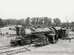 "Past and present in locomotives. Eckington Yards, June 4, 1923." A closeup of the locomotive seen here yesterday in the Baltimore &amp; Ohio rail yard during the Masonic convention in Washington, D.C. The big engine wears the livery of "Boumi Temple," a Baltimore Shrine lodge. 5x7 glass negative.  View full size.
Over a BarrelThe barrel more likely contained water for the boiler. There may have been a small box for coal, but small and early locos didn't stray too far from a source of fuel. Water was a bigger concern, so it was almost always carried on the engine or in the tender.
EL-3?By all accounts that is exactly a variation of the EL-3, except for that forward stack, which doesn't seem typical for the class. 
Amazing march of progressThe smaller locomotive is very interesting to see in detail. It says it was built in 1832; that makes it one of the earliest steam engines to run on rails in the country. But it was not the first; that honor corresponded to another 0-4-0 locomotive known as "Stourbridge Lion", which was built in 1828 and was imported from Britain. 
This is a very, very early design concept. A vertical boiler, two vertical cylinders, moving beams and shafts, inside "crankshaft" style axles -- this thing, in its time, was capable of pulling one or two small cars for short distances and at a very low speed, but it must have been an impressive sight to behold! 
I wonder if they took more pictures of that old locomotive.
EL-1B&amp;O 7100 was an EL-1 class 2-8-8-0 Mallet compound, built by the Baldwin Locomotive Works in 1916 - the EL-1 classification is legible on the builder's plate in the full size view.  Subsequent EL-2, EL-3 and EL-5 class locomotives were very similar.  Most were converted to simple articulateds starting in 1927.
More On These LocomotivesThe 7100 is class EL-1, built by Baldwin in 1916.
The little engine is the Atlantic, but it really isn't the Atlantic.  The original Atlantic was built in 1832, taken out of service in 1835 and scrapped. This locomotive was originally named the Andrew Jackson.  These engines were called grasshoppers in early parlance because of their drive mechanism, and the Atlantic was the first of them.  The A. Jackson was the only one left by the 1890s, when B&amp;O wanted to send an early locomotive to the world's Columbian Exhibition, so they turned the Jackson into the first grasshopper, the Atlantic.  It now resides in the B&amp;O museum. The original Atlantic was built in 1832, of 2-2-0 wheel arrangement, and weighed 6.5 tons. The is an 0-4-0 built in February of 1836.  (Source: B&amp;O Power, Sagle and Staufer, 1964)
Shriners and MasonsJust some clarification from one who has traveled east, and also travelled over the hot sands.
Masons belong to Lodges.  Shriners belong to Temples.  All Shriners are Masons, but all Masons are not Shriners.  These cars and locomotives hauled Shriners to a convention of some sort.
No, we do not and never have secretly or openly ruled the world.
Single smokestackThes engines were Mallet-system compounds when built, with a single blastpipe and smokestack. When they were converted to single-expansion engines they were fitted with dual blastpipes and stacks:
http://www.northeast.railfan.net/images/bo7120s.jpg
Fuel barrelI assume that the barrel was filled with coal for the vertical boiler. I wonder where the engineer stood to operate this engine, it was probably dangerous as all hell with the exposed operating mechanism.
The Pioneer     The wooden passenger car in the middle right edge of the photo is a replica of the 'Pioneer'. 
 From the B&amp;O website:
"When the B&amp;O began operation in 1830, its trains were pulled by horses. Constructed by Richard Imlay, the "Pioneer" was the first passenger car on the Baltimore &amp; Ohio and was one of the first passenger cars produced in the United States. The "Pioneer" carried the B&amp;O board of directors on the railroad's first run to Ellicott Mills on May 22, 1830. In 1836, the B&amp;O stopped using horses to pull trains, but kept horses in its stables at Mt. Clare until the 1880s to pull cars through the city. The original "Pioneer" was scrapped at an unknown date. A replica was constructed by the railroad in 1892 for the World's Columbian Exposition. It was also displayed at the 1927 Fair of the Iron Horse."
     Another replica of the Pioneer is on display at the B&amp;O Railroad Museum:  Ellicott City Station.  The station is the oldest surviving railroad station in the US.
www.ecborail.org
(The Gallery, D.C., Natl Photo, Railroads)