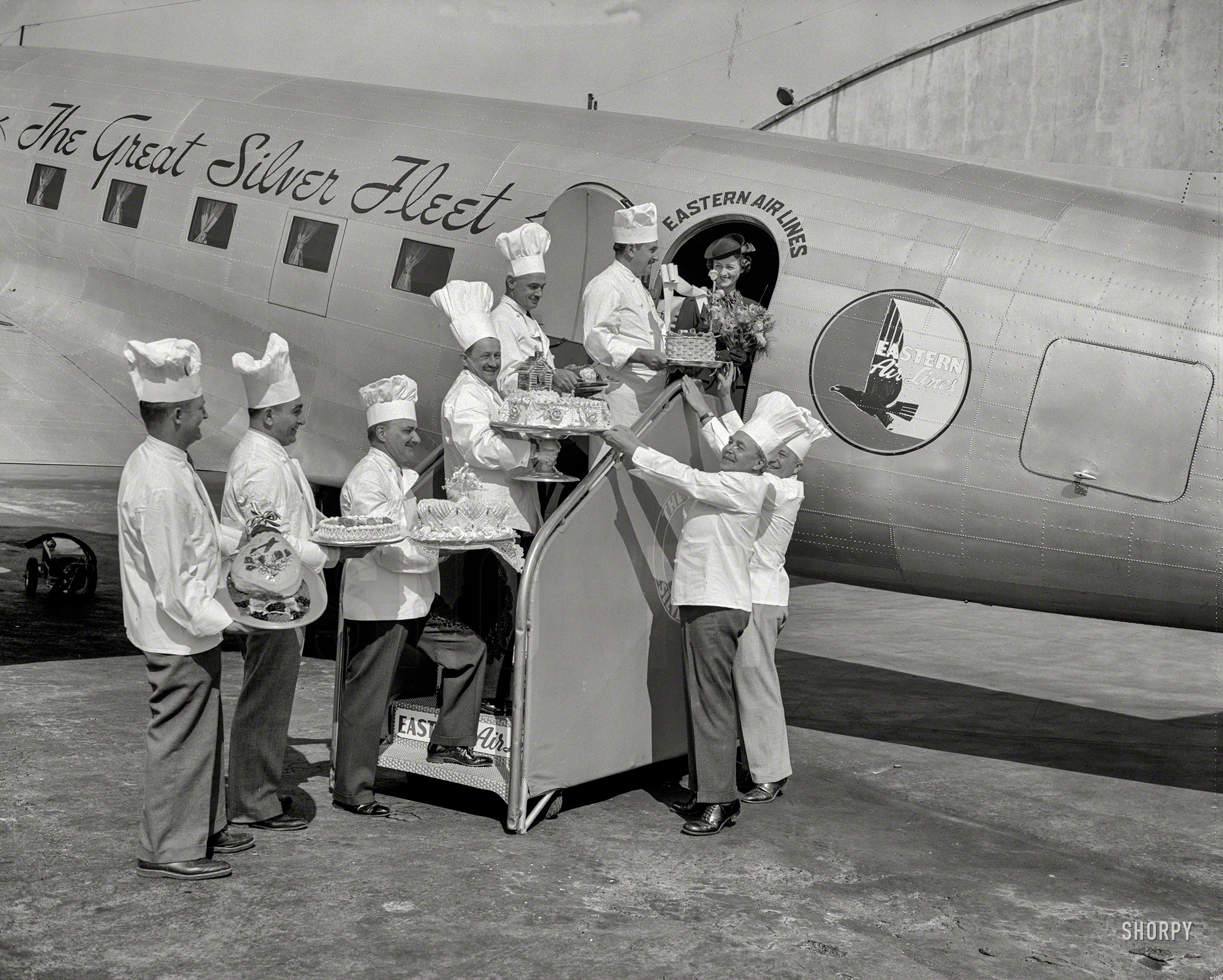 October 4, 1938. "Cakes for sky riders. Air travelers leaving Washington Airport during National Air Travel Week, Oct. 2 through 9, are being given a special treat. Cakes baked from their favorite recipes are being put aboard each plane by chefs of the leading hotels in the Capital. Marjorie McKinnon, Eastern Airline hostess, is pictured receiving the delicacies from (left to right) Theophile Homberger, Hotel Hamilton; Eddie Weber, Shoreham Hotel; Joseph Cattaneo, Hotel Washington; Fritz Meissner, Hay-Adams; Abraham Grob, Wardman Park; Joseph Tucci, Raleigh; Jacques Haerringer, Shoreham; Otto Merz, Willard." View full size.