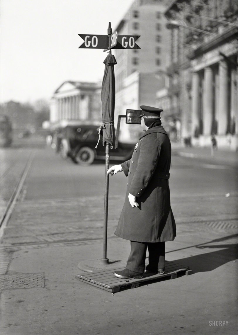Circa 1919. "Traffic officer at 14th Street and Pennsylvania Avenue." Before stoplights in the District of Columbia, there was the "Go-Go" traffic sign equipped with umbrella and rearview mirror. The Willard Hotel and U.S. Treasury play supporting roles in this Harris &amp; Ewing glass negative. View full size.
