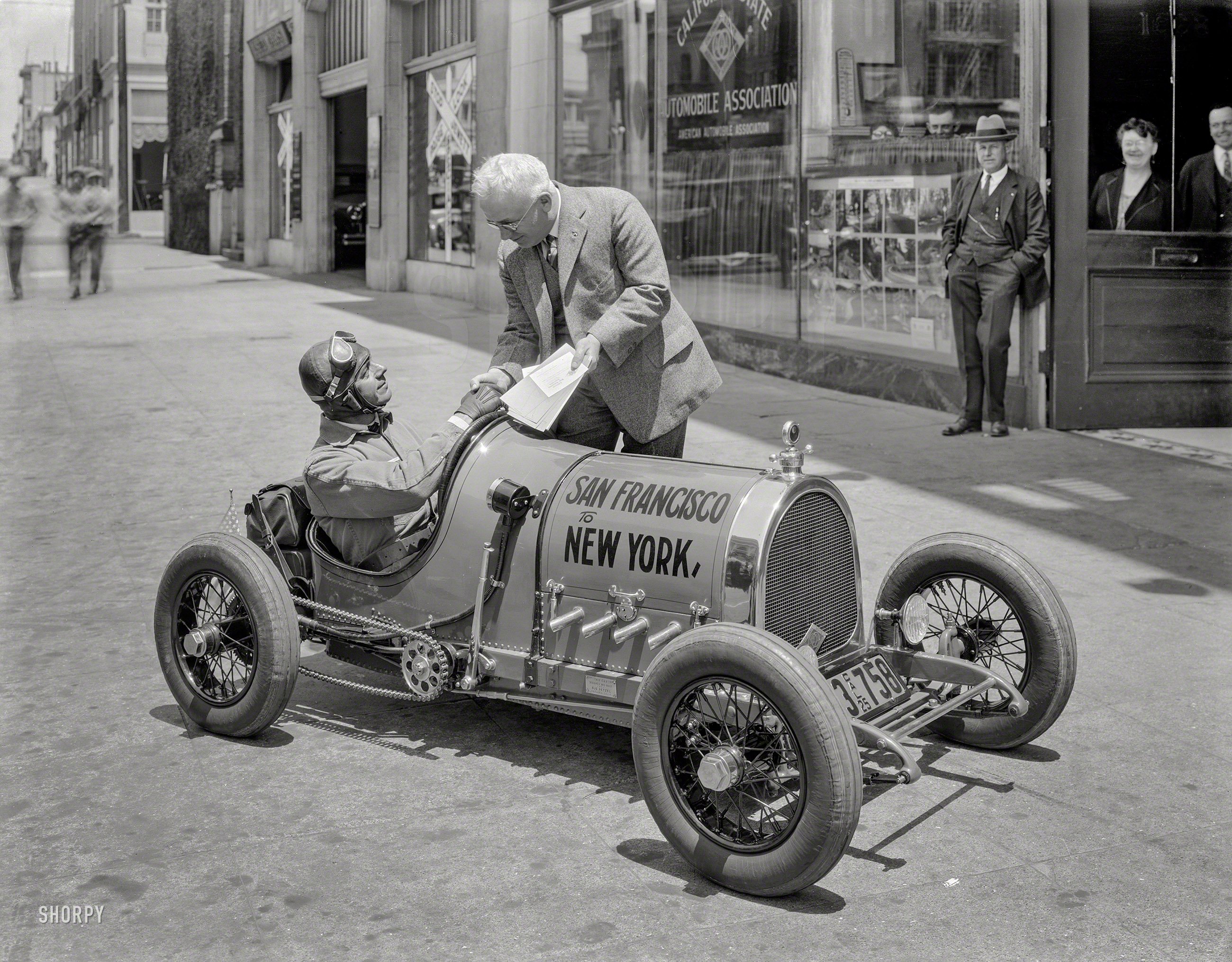 &nbsp; &nbsp; &nbsp; &nbsp; The smallest automobile in the world –- Designed and built by Gus Petzel of Alameda, California. The car has a 4-cylinder air cooled motor, 3 speeds, electric lights and starter, 60-inch wheelbase, 21x4 airplane tires, and weighs 560 pounds. It makes 52 miles per gallon and has a speed of 65 miles on the road and 80 miles on the track. Cost $2,000 to build. -- Promotional postcard
San Francisco, 1925. "California State Automobile Association -- Gus Petzel 'Baby Car' at start of cross-country run." A scene from the inauguration of the historic Trans-Continental Sidewalk. 8x10 nitrate negative. View full size.