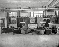 Washington, D.C. "Industrial exposition, 1926. Standard Upholstery Co." National Photo Company Collection glass negative. View full size.
AsisReminds me of second-hand stores of the 1950s. I can almost smell the mildew - wait, maybe that's coming from the negative.
Dome Fuel truck IDWhite
Furniture of a Better Kind


Washington Post, February 25, 1926.

Exposition to Show Big Range of Products


Washington-made products, ranging from candy to motor trucks, will be on exhibition at the second annual industrial exposition of the Washington Chamber of Commerce, to be held in the Washington Auditorium, March 4 to 13.

&#8220;The exposition is planned to give Washingtonians further reasons for civic pride,&#8221; Martin A Leese, president, said yesterday. &#8220;It should surprise any resident of this community who visits the exposition to see the number of food products, household appliances, wearing apparel and office fixtures which are made in this city.&#8221;




Washington Post, January 21, 1924.

Standard Upholstery Store
2810-12 14th St.
&#8220;Furniture of a Better Kind&#8221;


Overstuffed Furniture, Made to Order, 3-Piece Suite $125 up.
Furniture reupholstered and repaired. Draperies and Interior Decorating.

Sufficient unto the dayIs the stuffing thereof.  Who, exactly, determines that furniture is over stuffed, as opposed to "sufficiently stuffed" or even "scantily stuffed?"  Probably once a term of art in the upholstery trade, appropriated for vulgar use much in the way that the rubrics "stainless steel appliances," "granite countertops," and "open concept" have become indispensable narrative terms without which no home improvement TV show can long survive.
[The term "overstuffed" simply refers to furniture in which the frame is completely covered with padding and fabric, as opposed to, for example, an armchair with upholstered seat and back, but with wooden arms and/or legs. -tterrace]
And now I know!
Decorating trendI have never seen that style of upholstering before, with the tops of the cushions a lively print and the rest of the couch solid velvet.  It looks untidy now, but it may have been more practical in the days before sturdy synthetic fibers to have the sitting surface made from a more durable fabric than velvet.
(The Gallery, D.C., Natl Photo)
