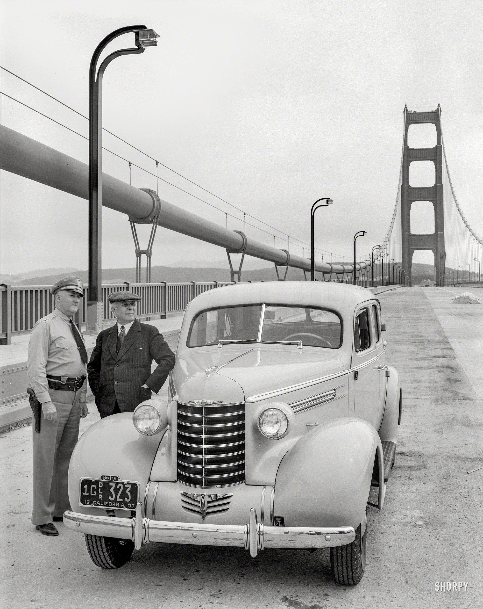 San Francisco, 1937. "Don Lee Oldsmobile on Golden Gate Bridge with police officer." Whose cruiser we can see reflected in the bumper. 8x10 acetate negative, originally from the Wyland Stanley collection. View full size.