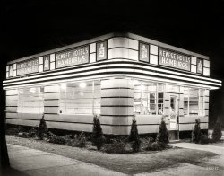 Circa 1930s. "Kewpee Hotels hamburger stand." This early fast-food chain ("Hamburg / Pickle on top / Makes your heart / Go flippity-flop") got its start in Michigan in the 1920s. Location and photographer unknown. View full size.
A Clean, Well-Lighted PlaceThe old short story by Hemingway is the first thing that popped into my head when I saw the photo, though I can't imagine the name "Kewpee" is one he would have approved of.
Hard to findIt might be hard to nail down the location. There were 400 Kewpee franchises by 1940. Some locations shut down during WWII because of meat rationing; others closed in the 60's when the new owners demanded stricter franchise agreements and a cut of profits. There are still five locations, including three in Lima, Ohio -- they must love their olive burgers in Lima.
Dave Thomas ate Kewpee burgers as a child. When he founded Wendy's, he replicated their square burger. He didn't offer Kewpee's olive topping.
Moon BurgersMy father and uncle started an ill-fated hamburger chain in the late 1960's. Moon Burger was their attempt to cash in on the public fascination with the Apollo "moon-shot" program (that's what Pops always called it).
The restaurants were tiny - built to resemble Apollo lunar landing modules. They were primarily drive-up joints, but had a few cramped stools inside. You placed your order with a Robbie-the-robot looking device a few yards away from the building. I think they tried some type of radio gizmo in the order-taking machine - never really worked that well. Folks just jabbed at the buttons for a while and then drove up to the window.
This was East Texas folks, hot as two rats in a wool sock. The metal-clad structures were tiny and not well ventilated - think Airstream trailer on it's end. I'm going to try to find photos - know they're somewhere.
The kicker was the Moon Burgers themselves. The cutting edge of interplanetary cuisine consisted of a 1/4 lb meatball encased in a moist doughy bun and deep-fried. After scooping it out of the fryer, green-tinted "cheese" was injected into the bun and it was wrapped in paper and served with fries and Coke. The damn things were so hot! That melted "cheese" and deep-fried beefball adhered to the roof of your mouth and sizzled. It was impossible to vent the "cheese" because once it started oozing out it stained everything it came in contact with. Never knew what they used to tint the "cheese".
I remember at some of the "grand openings" they gave away little slide-wheel calculators that revealed your "weight on the moon" when you rotated the device to your Earth-weight. Wish I still had one.
Moon Burgers never quite caught on. Though they didn't really become the hoped-for official fast food of the Age of Aquarius, one can still see some of the lunar landing modules posing as concession stands at the Louisiana State Fair.
As I enter my 7th year as a member of the Shorpy community I offer many, many thanks to Dave, tterrace, and all who make this site possible. I'll plug Juniper Gallery - their prints make great gifts and office adornment. When I need a little perspective I amble on over to Shorpy to look back in time for a while. Can't say there are any profound answers lurking in these images and comments - but there sure are a lot of great questions.
Wish me a happy Shorpy anniversary!
Goober Pea
PickleAs Mr Kitzel would say, "the pickle in the middle with the mustard on top", although that was for hot dogs.
At Last, the Answer!I was born in Lima, Ohio, and lived there until I was almost four years old, my father being at the time engaged in an all-expense tour of places like Bougainville and the Philippines.  I have always had a vestigial memory of a strange building I saw on walks with my mother or grandmother, but neither of those worthies in later years seemed to know what I was talking about.
When I saw this photo, it was as if the intervening 67 years had never happened and, thanks to archfan's comment, I now know that what I dimly remembered was a Kewpee Hotels Hamburger stand.
Thanks, Dave!  Thanks, archfan!  Thanks, Shorpy!
HamburgsIn my experience, "Hamburgs" pegs the chain to Michigan or northwest Ohio, even without reading the caption.  I know of nowhere else that America's favorite sandwich is a two-syllable word.
A Racine VestigeAccording to the information here, the Racine, Wisconsin Kewpee is one of five remaining restaurants in the chain. I have eaten at this location and can say that the food is good and that there is always a line of people waiting to get seats. Attached is a photo from my July, 2010 visit.
HamburgsThe area around Rochester, NY is (or was when I lived there) another in which hamburg prevails over hamburger.  And hot dogs are simply "hots," and come in red and white.
&quot;Hotels&quot;Any reason "hotels" was used in name?
[The Kewpee Hotel in Flint, Michigan, is where the restaurant is said to have gotten its start. - Dave]
Kewpee dolled up with a HaloThe Kewpee chain started in Flint, Michigan, and evolved in to what is now known as Halo Burger. Under recent new ownership, the chain is starting to expand in southeast Michigan.
I was introduced to it by a girlfriend who liked the olive burger. Every so often I need a Halo Burger fix and I used to have drive over an hour to get one. Now I only have to drive about 30 minutes. 
Kewpees There was one in Grand Rapids. Grandma took us there a few times when I was a kid. It's where I developed my love for olive burgers! There was also a Wimpy's nearby; sadly they both closed before I was old enough to go there on my own.
(The Gallery, Eateries & Bars)