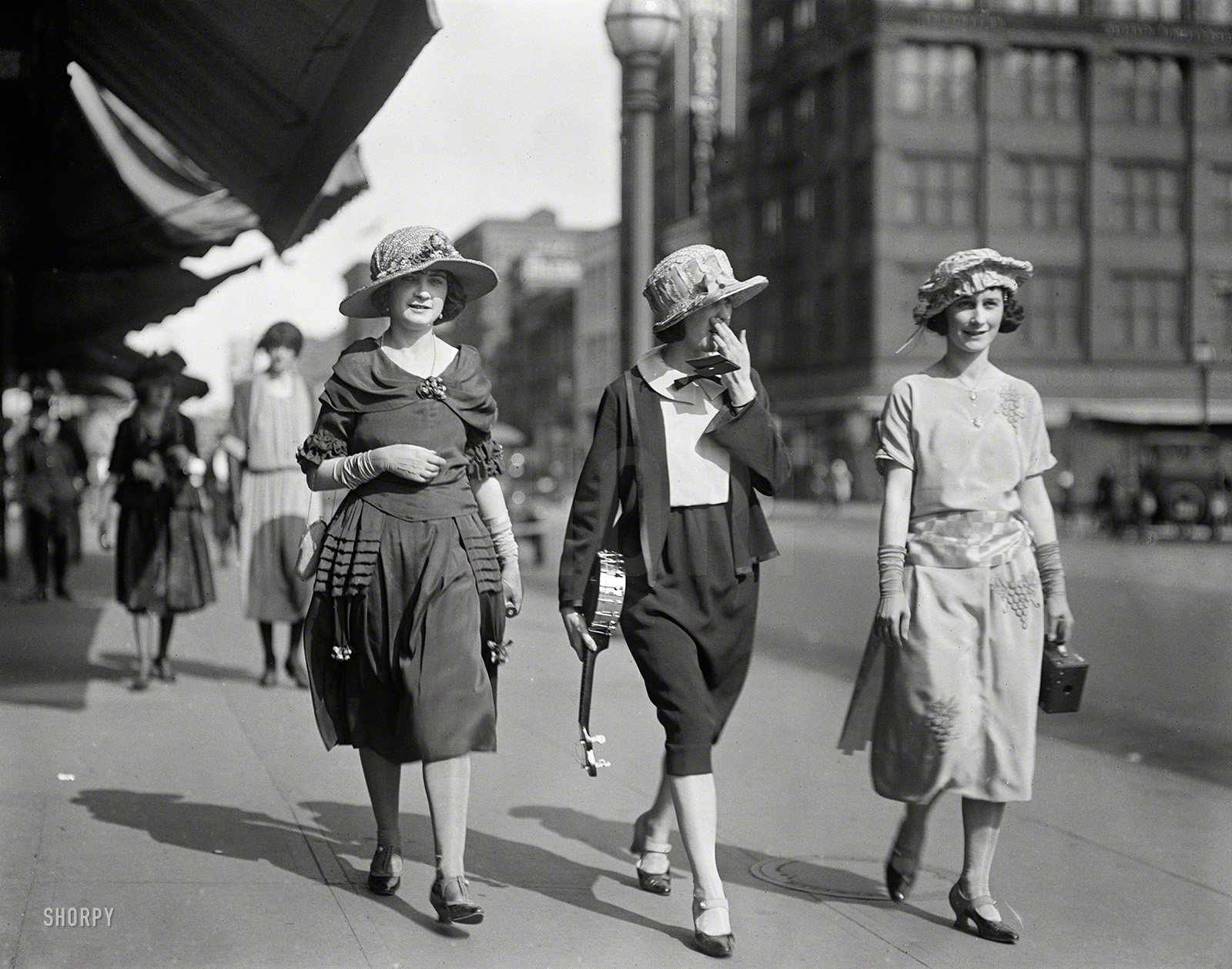 Washington, D.C., 1922. "NO CAPTION (women on street)." One in a series showing spring fashions at Easter. This trio is going places with a camera and a banjo. Harris & Ewing Collection glass negative. View full size.