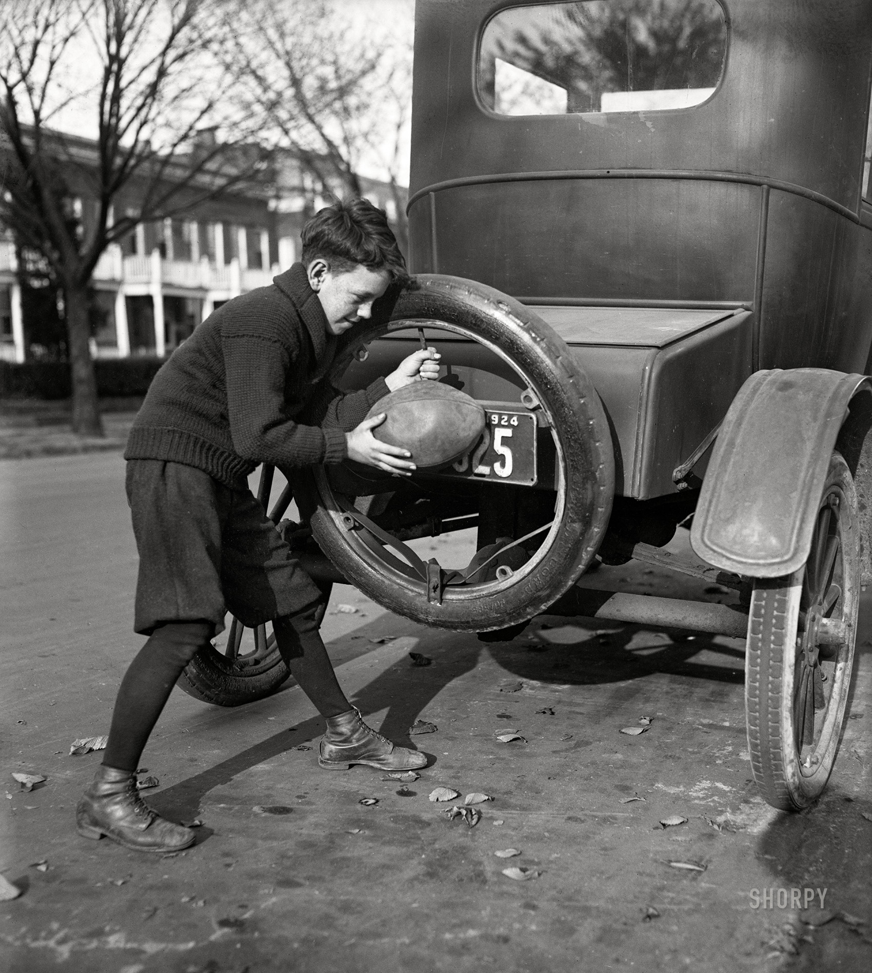 Washington, D.C., 1924. "Flat spare tires are numerous around Washington these days due to the youthful football players who have found an easier way to inflate the pigskin than using their lungs. 'Billy' Friel shown inflating his football." 4x5 inch glass negative. View full size.