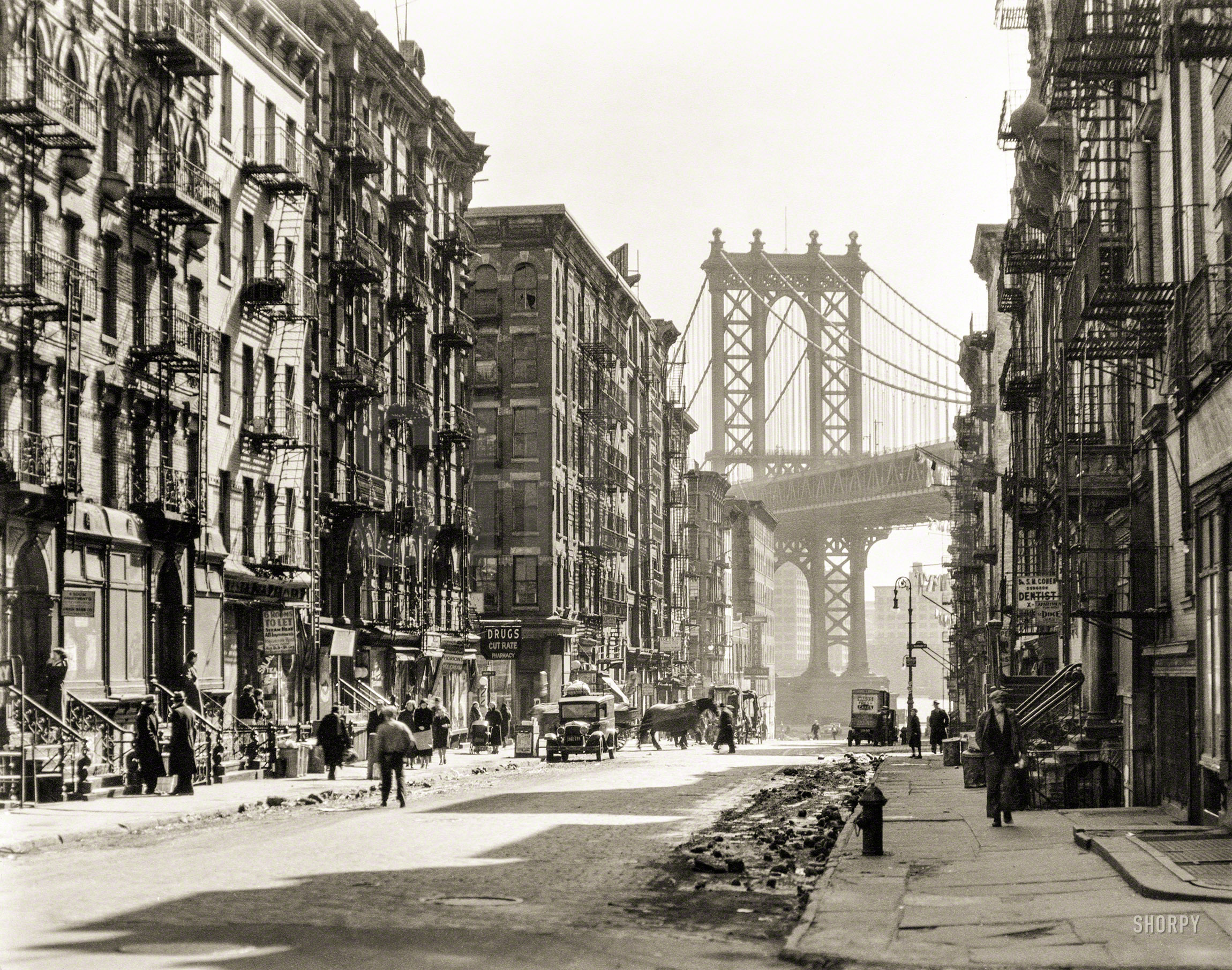 March 6, 1936. "Looking down Pike Street toward the Manhattan Bridge, street half in shadow, rubble in gutters, some traffic." 8x10 gelatin silver print by Berenice Abbott for the Federal Art Project. View full size.