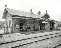 Circa 1899. "R.R. depot at Garrison, New York." En route to their final destination. 8x10 glass negative, Detroit Photographic Company. View full size.
Beautiful locationThe Metro-North Hudson line runs along the Hudson River up to Poughkeepsie. A truly beautiful train ride around sunset.
Chair legs I'd venture a guess that the fellow second from right is the telegraph operator, due to the fact the chair he is sitting in has glass telegraph insulators on the front legs.
I have heard of rangers on watch duty in forest fire towers and telegraph operators doing that in case of a lighning strike, but they would put them on all four, not just the front ones.
Insulated leg extensionsIt looks like the young man sitting on the left has his chair propped up on some telegraph pole insulators. I would imagine they have a few boxes stored there. 
Dressed upGranted that people dressed up to go anywhere in those days, but the level of best-of-the-Sunday-best sort of suggests a trip to NYC itself.
Bolivia BoundButch Cassidy leans nonchalantly agains the window sill while Sundance assumes an agressive stance to his left.  Their traveling companion, Etta Place, has just went inside to buy their tickets.
Hello DollyThe Garrison train station is used as the set (standing in for Yonkers) in the movie Hello Dolly.  Lots of information if you scroll down to "Garrison New York Location" here.
New York Central RailroadBeing that Garrison Station is now Metro North RR today this means it is a very good probability that at the time of the photograph this was a New York Central Railroad Station.
RevolutionaryNew York City 50 miles this-a-way (south), and Boston 390 miles that-a-way (northeast).
BTW, called Garrison, because General Washington garrisoned his troops there as a blocking force to protect control of the Hudson River while the British occupied 50 miles this-a-way (south) aka NYC. If the British got control of the Hudson, they would have had a wedge between New England and the remainder of the 13 colonies.
B is for BuffaloThe "B 390" stands for Buffalo, NY, not Boston.  The New York Central did eventually reach Boston, but via a subsidiary railroad called the Boston and Albany (which it didn't assume control of until a year after this photo was taken).  Milepost measurements are from NYC to Buffalo and eventually Chicago (when you include their Michigan Southern subsidiary).
Today Garrison itself still has a rural feel to it, but this station building is long gone, replaced by modern high-level concrete platforms.
(The Gallery, DPC, Railroads)