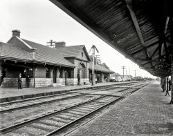 Circa 1899. "Chicago &amp; North Western Railway station, Elmhurst, Ill." 8x10 inch dry plate glass negative, Detroit Publishing Company. View full size.
Another Left Handed RailroadThe Duluth Missabe &amp; Northern, later incorporated into the Duluth Missabe &amp; Iron Range, now part of the Canadian National, also considered itself to be a left hand railroad.  On double track, trains ran on the left hand track, and all signals were placed to the left - even on single track.  Some of these signals still remain.
Tie PlatesThere are no tie plates to spread the load of the rails to the crossties (sleepers to our European friends). Some of the ties look the worse for wear because of this. According to Wikipedia, tie plates came into use around 1900, just about the time of this photo.
It izIt is indeed the tap for the circuits into the station; but a bit more than that. I can see five lines which can be opened - see the insulators on bars, so the wire comes in from (say) the east, runs into the station, comes back out, and heads west. That is, the wire is not continuous past the station, but both sides go into the station. 
I would expect that the box contains primary lightning arrestors for each wire dropping into the station; secondary arrestors may be in the station.
With this arrangement, circuits can be patched from one wire position to another. Also remember that telegraph was the usual communication system at the time of this picture.
It iz....answersignalman,
Thank you for the info!   Makes sense now.   I wonder if the 'thick' wire is just a thick ground or contains the two lines headed down to the station.   I would think it as a ground as it is just too thick for two small lines.
WhatizitSo my family and I have extensive telephony background, and personally I have that and railroad background, but still, what is the item on the telephone crossarm that looks to be rectangular, about 3 feet long with a pitched roof with one thick cable exiting the bottom?   Is there a name for this and what is its purpose? 
I agree there are lines going from the insulators into it, so it may be some sort of permanent tap for the stations telegraph/telephone.  Even so, seems to be overdone for a simple splice.
As a child I used to take the train there... on Saturday mornings in the winter to play ice hockey at the YMCA several blocks away. Where did those fifty years go?
A Scratch-builder&#039;s ParadiseIf you model train scenes, in any gauge, this picture is a veritable goldmine! Such wonderful details would keep the poor modeler busy for many a snowy evening. Positively stunning. Keep up the good work.
Left-Handed Train Operations on the C&amp;NW RailwayIn the deep background you can just make out two trains that illustrate one of the most peculiar features of the Chicago &amp; North Western Railway, the fact that its trains operate on the left hand track, rather than the right hand track. This practice continues to this day, which makes the C&amp;NW (now part of the Union Pacific system) the only left-handed railroad in the USA. The explanation for this unusual practice usually goes like this:
"The first component of what was to become the Chicago &amp; North Western Railway was the little Galena and Chicago Union Railroad Company. Tracks were laid west from Chicago to Geneva, where the first station was to be built. The company built the station on the north side of the tracks where most of the people lived. This saved passengers the inconvenience of having to cross the tracks to go home.
When traffic required double tracks, the only place to lay new rails was south of the original single tracks. Since the stations were used primarily by passengers waiting to travel into Chicago, the company decided to run east-bound trains on the old track so riders would not have to cross the tracks to board—a dangerous process." (From Tom Hermes, "Why Does Our Train Run on the Wrong Track?" Winnetka [Illinois] Historical Society Gazette, Fall 1996, reprinted at www.winnetkahistory.org)
(The Gallery, DPC, Railroads)