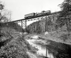 Circa 1900. "Detroit Photographic car crossing DL&amp;W bridge over the Passaic at Millington, New Jersey." 8x10 inch glass negative. View full size.
DL&amp;WThe initials meant delay, linger and wait, according to my commuter father in the 50s, apparently a current joke.
Push it real goodIs the passenger car in this photo being pushed by the engine, rather than pulled? And if so, why?  
NJ TransitThe bridge has been replaced by a girder type, but the line is still in use by NJ Transit on the Gladstone Branch.
Push or pullWell, at the moment, the train is stationary - you can see that the engine crew are watching the photographer do his work.
Locomotives work equally well in either direction, and pushing a short train is not a problem either, so there is no way of telling which direction they have been or will be traveling.  The opportunity to turn an engine is only found at large terminals with a turntable, or at "wye" intersections, so it was and is sometimes unavoidable to have the engine running tender-forward. Furthermore, passing sidings are also not located very close together, so it may happen that pushing the train is unavoidable. 
Push-You-Pull-MeI've become aware of a very short line called the Emittsburg railway that was built when the town learned that the Western Maryland Railway was going to bypass it. So the town financed its own seven-mile, single-track line from Emmitsburg south to meet the new rail line at Rocky Mount. As a single line, it was designed so that the engine always had to run in reverse on half of the trips.
(The Gallery, DPC, Railroads)