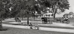 Chicago circa 1907. "Jackson Park -- Driveway and Field Museum." Formerly the 1893 Columbian Exposition's Palace of Fine Arts; today the Museum of Science and Industry. Detail of glass negative by Hans Behm, Detroit Publishing Company. View full size.
When beauty IS skin deepIt's not  quite the same building today: the exterior was originally a semi-permanent material  ("staff") and had to be rebuilt for the Museum  It's hard to tell but it looks like it might already be deteriorating in the picture.
Car ID1904 Winton (with luggage rack on roof)
Gentler, for sure!Shorpy should have a category just for Willoughbies!
A Gentler TimeI want to walk into the photo, cross that lawn in the summer sunshine—avoiding the sprinklers, of course—visit the museum, and leave the 21st century behind.
A wondrous placeWe spent many happy hours at the Museum of Science and Industry with our children when they were youngsters.
Yesterday in the Park --I think it was the Fourth of July.
Dog Gone Amazement ...I noticed the dog looking at one of the cars going by. He, like the people, seemed fascinated by the new contraptions rolling down the road. In 1907, the automobile was still a modern marvel. Our society was gradually transitioning from the horse and buggy to the automobile. When Henry Ford began mass producing the Model T, on the assembly line, the automobile quickly replaced the horse and buggy. That happened not long after 1907.
Thank you, Dave, for all the neat photographs from history you have posted on this site! We all have the opportunity to get a glimpse of the past thanks to the person who took the picture. I'm glad this photograph captured the handsome dog, standing by his owner, looking at the car. He may have been one of the first dogs in history to chase a car!
Smell v. SightI believe the dog is looking at the horse, not the car. Of course, a dog's sense of smell is more important to him than his vision or hearing and the horse's smell is probably more interesting to him than the car's. The car is just a smelly nuisance.
(Panoramas, Cars, Trucks, Buses, Chicago, Dogs, DPC)