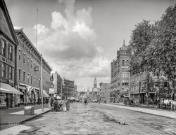 1908. "Main Street -- Nashua, New Hampshire." At right, offices of the Nashua Telegraph and Fletcher's Optical Parlors. 8x10 inch glass negative, Detroit Publishing Company. View full size.
1908 and 2017
PigeonsJust try to tell me pigeons aren't trash birds!
Safe spaceMaybe you heard this already but WalletHub just named Nashua, New Hampshire, the safest city in America. The other nine in the top ten are Columbia, Maryland; South Burlington, Vermont; Gilbert, Arizona; Warwick, Rhode Island; Portland, Maine; Casper, Wyoming; Yonkers, New York; Burlington, Vermont; and Scottsdale, Arizona. 
According to the same study, South Burlington, Vermont (the third safest city), "also tied with Cleveland and Cincinnati, Salem, Oregon, Washington, D.C. and Seattle for the most hate crimes per capita." Uh oh. Maybe move to Burlington, Vermont -- less than three miles away and coming in at ninth on the safest city list.
Or just stay put and take your chances.
CLOUDS!I don't know if it was luck or some type of different exposure process, but it's rare to see a sky with clouds in these old photos. The cameras couldn't pick up the subtle shades and usually the skies appear completely white even though at the time they may have been overcast or partly cloudy.
Because now you can bank onlineWorking left-to-right: 
JennyPennifer's comment caused me to pay special attention to the police officer walking his beat, just to the left of the wagon parked at the curb.  He's dressed like a London Bobby.
The four-story building with the curved front is, regrettably, gone.  This likely happened when Main Street was straightened, and a newer bridge was built across the Nashua River. The Romanesque church at the end of the street is on the other side of the river.
The building at right, which became a bank in jrpollo's update, is now luxury condos, called The Mint.  Not to criticize too much, but my first efficiency apartment had more kitchen space. I guess the residents are expected to eat out. A number of nearby restaurants have expanded their al fresco option to include both the sidewalk and the parallel parking spaces in front of their restaurant.
Straight and trueI lived in Nashua for 12 wonderful years and lived in the North End right off of Concord. This image did raise a question about the curved building a block from the river crossing. Any straightening alluded to earlier would have taken place much earlier in the 19th century...
The Sanborn Insurance maps of 1912 indicate that Main Street and the bridge were already where they are today. But the curved building, identified as the Howard Block gracefully curved to widen the main street from the width of the bridge (I am guessing). Main Street really is three lanes wide in each direction... feels like an avenue in Manhattan. I am also grateful that the Library of Congress has these Sanborn maps...! Terrific detail about buildings and their particular use.
Here is the link to that image:  https://www.loc.gov/resource/g3744nm.g3744nm_g053631912/?sp=32&amp;r=0.517,0...
Different process = CLOUDS!Eary photographic processes were primarily sensitive to only blue light. Numerous newer processes throughout the late 19th century added increases sensitivity into the greens and yellows resulting in what we now call orthochromatic materials. 
It wasn't until around 1906 that a truly panchromatic emulsion with full sensitivity to red was developed. This took several decades to become dominant. It wasn't until the panchromatic films and plates became available that we begin to see photos that can render skies anything other than nearly blank white. 
Orthochromatic materials remained in use for quite a while largely because you could develop them under a red safelight. Panchromatic materials required total darkness.
[Here and here, some clouds from 1864! - Dave]
Light grey/white clouds against a blue sky require a panchromatic emulsion, otherwise the clouds and sky reproduce nearly the same light grey. Only when the clouds are all grey and dark grey (think: storm clouds) will they reproduce on earlier orthchromatic or pure blue sensitive emulsions.
Tea TimeThe Grand Union Tea Company delivery wagon in the Nashua photo made me curious. My local New Hampshire grocery store used to be a Grand Union. I found a brief history of the company here:
https://oldmainartifacts.wordpress.com/2013/10/07/grand-union-tea-compan...
(The Gallery, DPC, Small Towns, Stores & Markets)