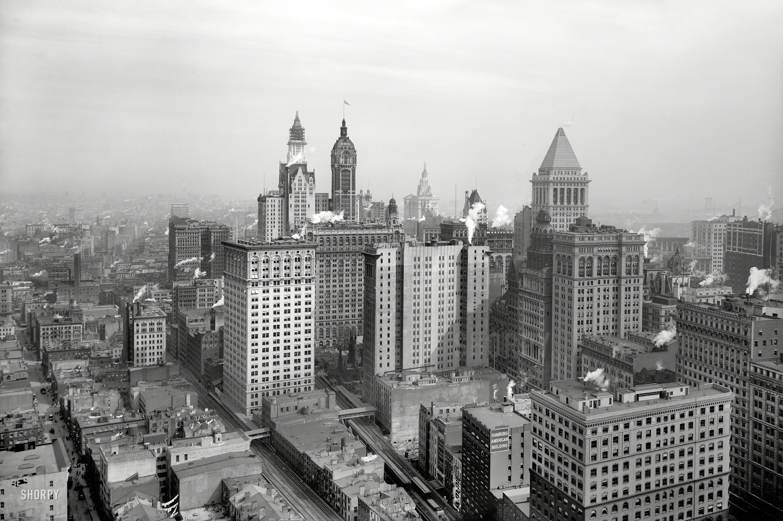New York circa 1912. "The big buildings of Lower Manhattan." Landmark skyscrapers in this view (from where?) include the Woolworth (left) and Municipal buildings nearing completion, as well as the Singer and Bankers Trust towers. Panorama made from two 8x10 inch glass negatives. View full size.