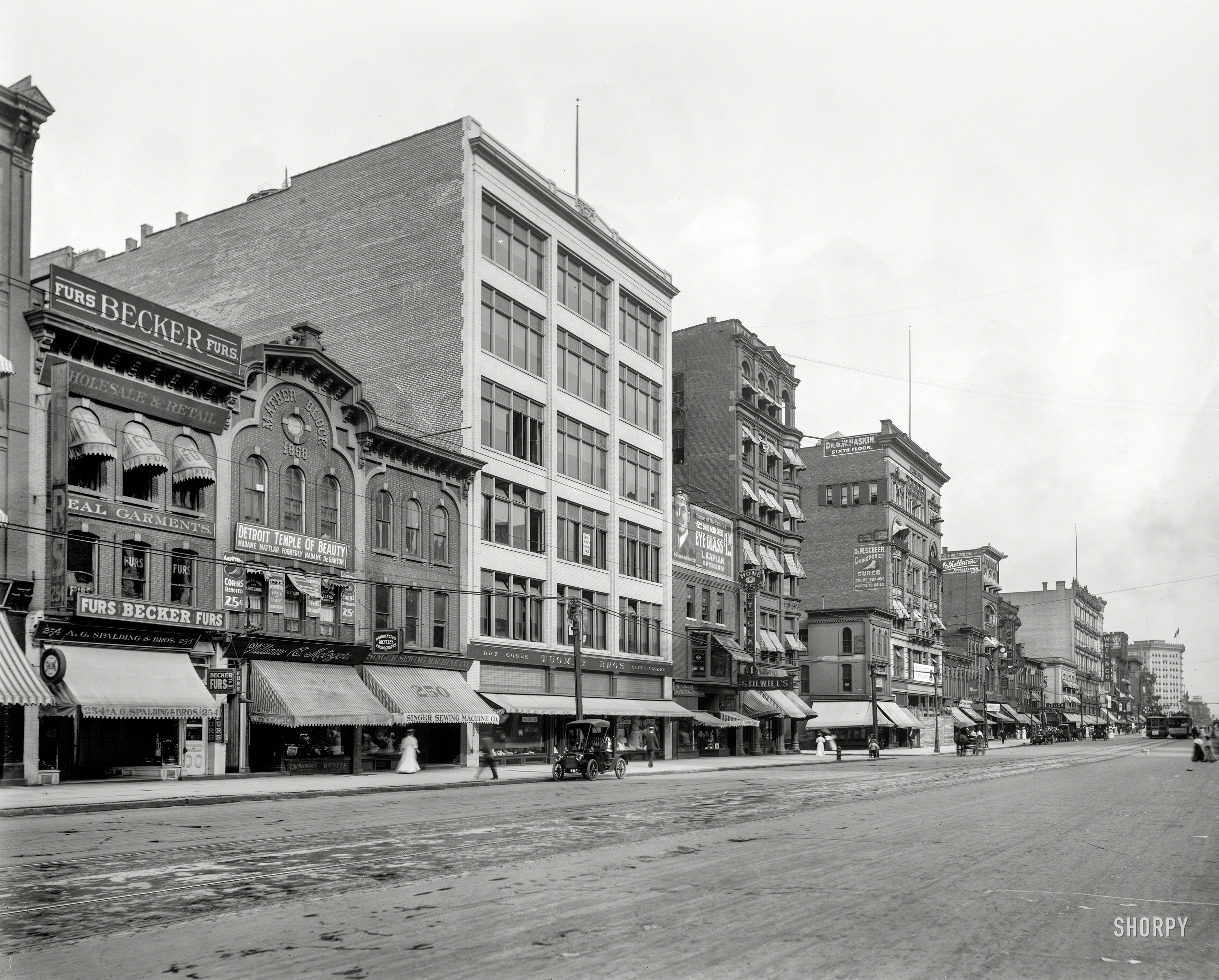 Detroit circa 1908. "Mather Block, Woodward Avenue." Where merchants vying for your trade include Madame Mattlar's Temple of Beauty ("Corns removed, 25¢"); William E. Metzger, dealer in "Motorcycles Bicycles Phonographs"; an outpost of the Singer Sewing Machine Co.; Tuomy Bros. (suits and cloaks) and the eyeball-bedizened offices of L. Kaplan Optician ("I Glassed Detroit"). 8x10 inch dry plate glass negative, Detroit Publishing Company. View full size.