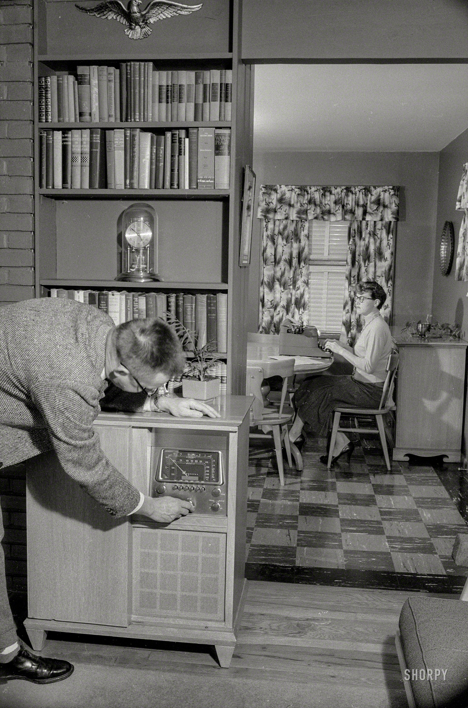 &nbsp; &nbsp; &nbsp; &nbsp; "Dick turned the volume up to 11 to drown out the sound of Mary's infernal pecking, while silently she plotted her revenge. Well, not really silently -- Mary was typing her plan at the kitchen table."
December 1957. Washington, D.C. "Man tuning console radio while woman in next room types." 35mm negative from the News Photo Archive. View full size.