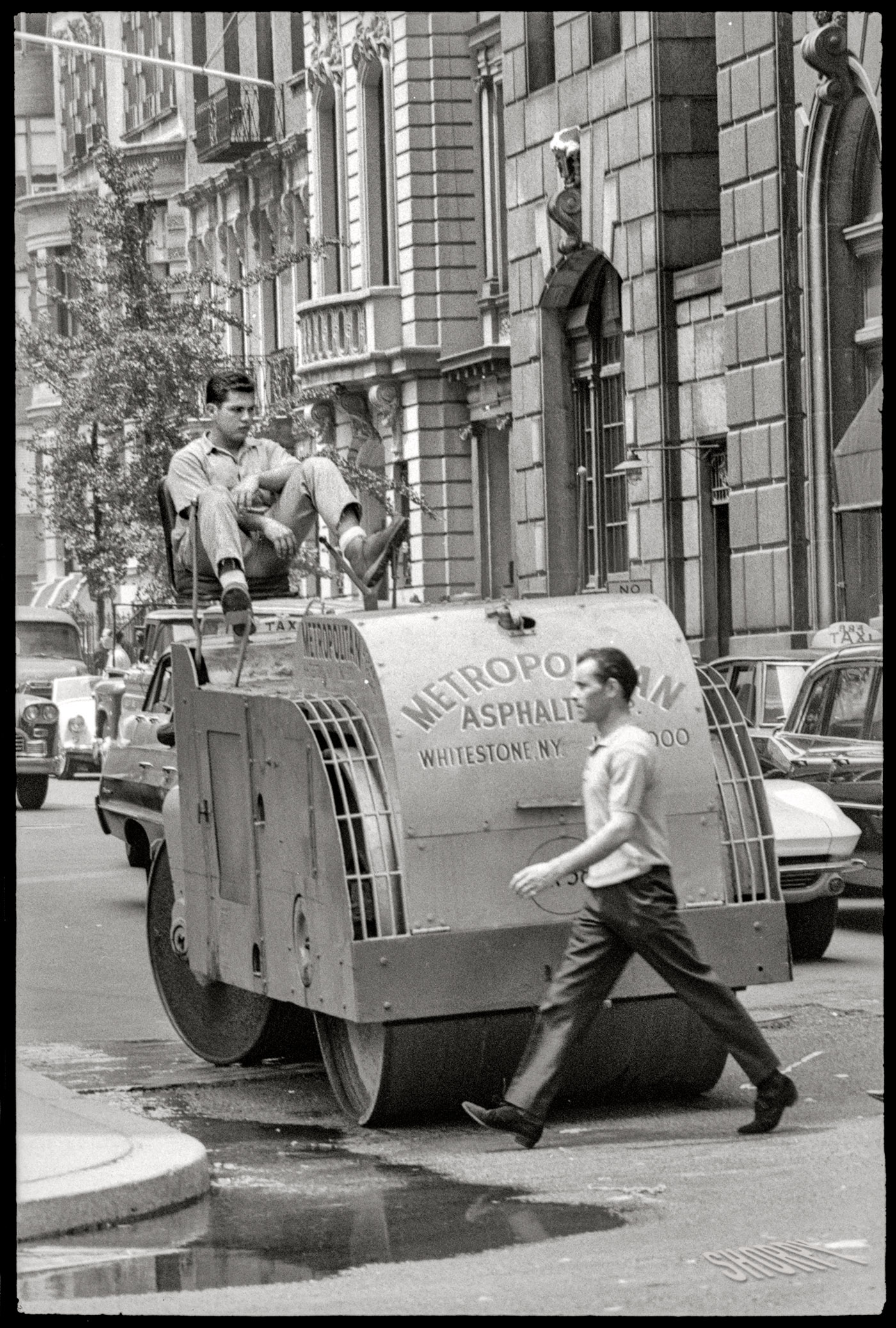 July 1964. New York. "Man walking in front of construction worker driving asphalt paver." From that day on, his friends called him "Stretch." 35mm negative by Angelo Rizzuto. View full size.