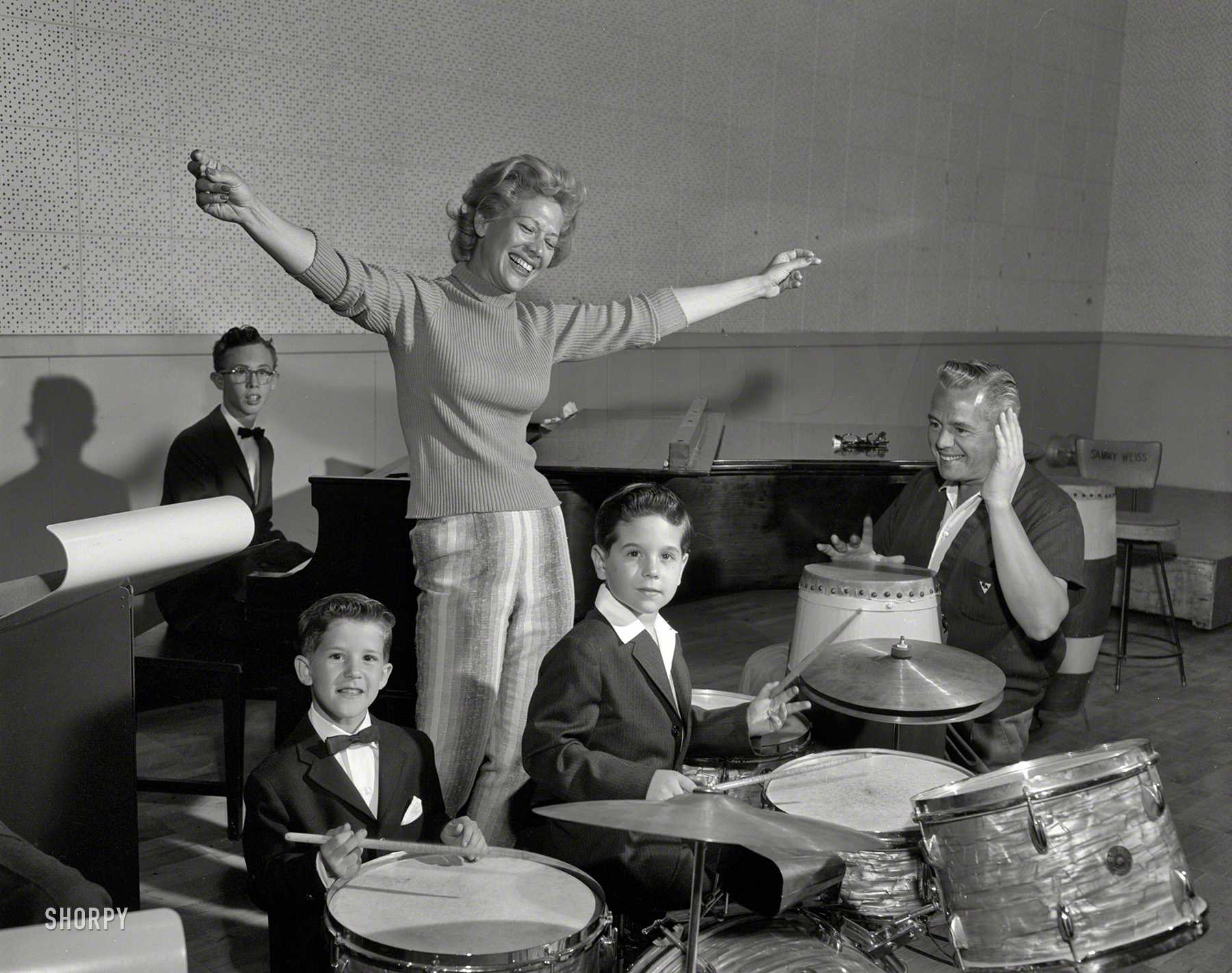 &nbsp; &nbsp; &nbsp; &nbsp; Sunday, April 3, 1960. 9 P.M. (NBC) -- Dinah Shore Show (60 min., Color). Guests are Betty Grable, Vic Damone, the Wiere Brothers and two youngsters -- Desi Arnaz IV and Richard Keith. The boys help form an all-child band.
Dinah Shore with Desi Arnaz, Desi Arnaz IV and Richard Keith on the set of her TV show in Los Angeles. 4x5 negative by Paul Bailey for NBC. View full size.