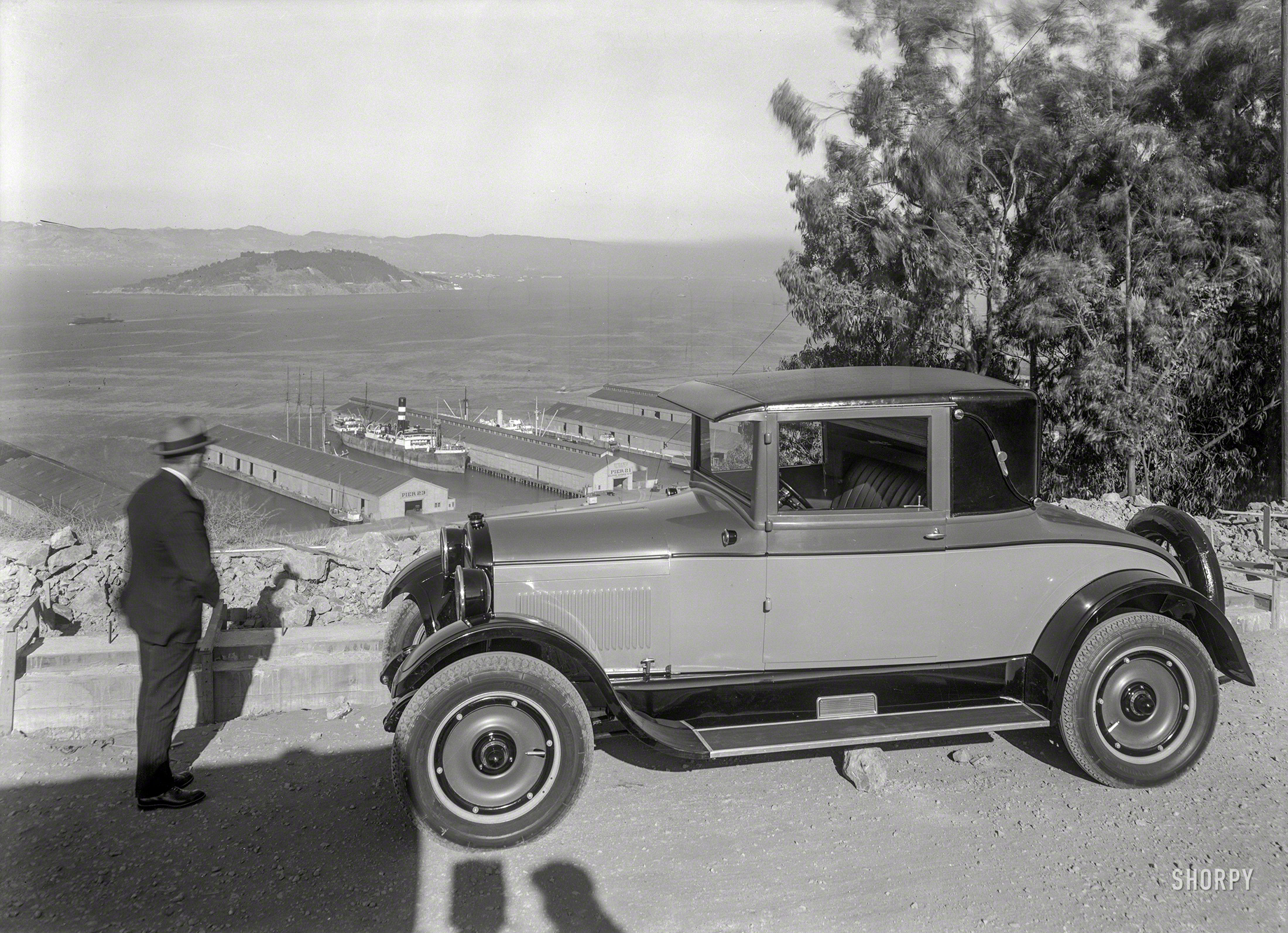1925. "REO coupe overlooking San Francisco Bay, Embarcadero piers and Yerba Buena Island." Plus an unintentional shadow-selfie. 5x7 glass negative, formerly of the Wyland Stanley and Marilyn Blaisdell collections. View full size.