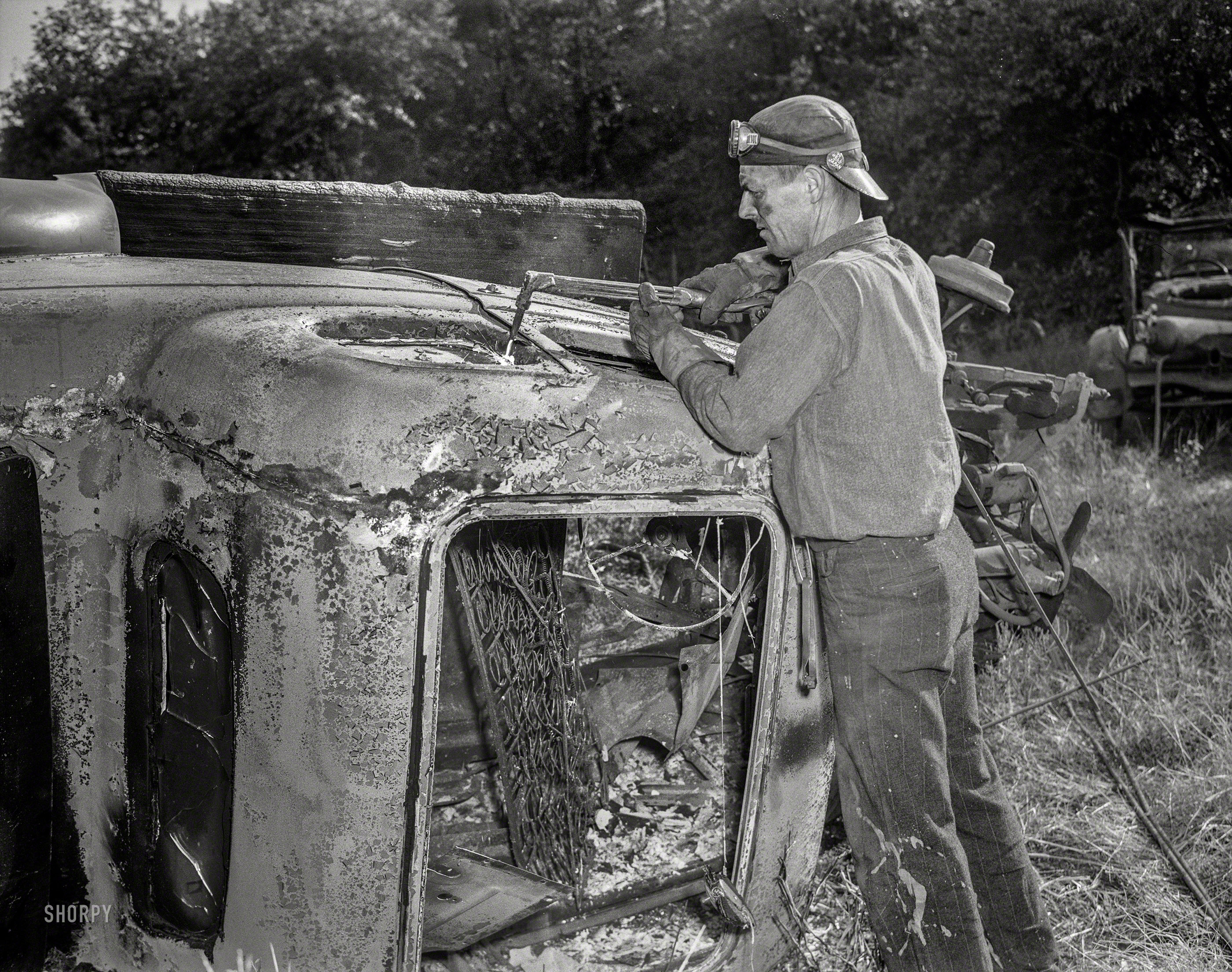 September 1942. "Automobile salvage. Automobile bodies are usually cut into four pieces so they can be readily loaded into a press for baling. The acetylene torch separates the lightweight body from the heavyweight steel frame of the car. Note: the auto has already been burned to remove all wooden parts, upholstery, oil, grease and other unusable and inflammable material." 4x5 nitrate negative by William Perlitch for the Office of War Information. View full size.