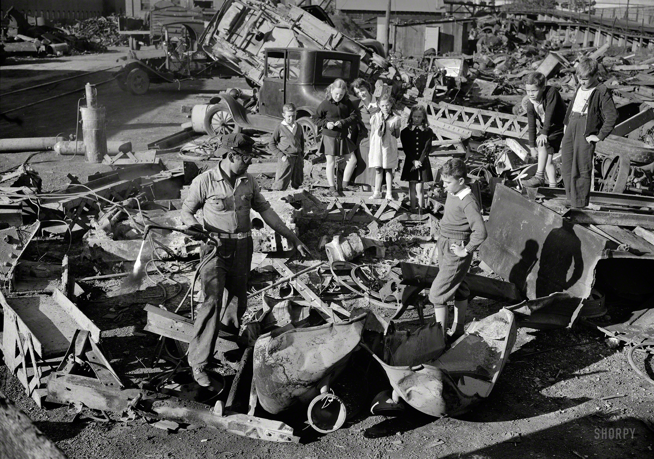 October 1942. "Manpower, junior size. Proud young fighters in Uncle Sam's junior army visit a scrap yard in Roanoke, Virginia, to see for themselves what happens to the scrap they collect for our war industries. One of the workers explains to the children how the acetylene torch he holds cuts heavy metal into the shapes required for melting by the steel mills." 4x5 inch nitrate negative by Valentino Sarra for the Office of War Information. View full size.