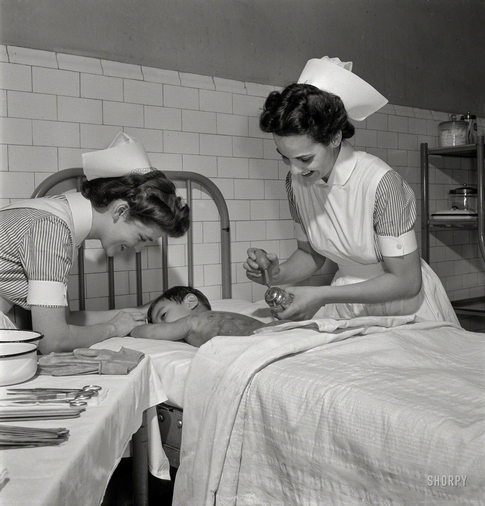 November 1942. Babies' Hospital, New York. "Nurse training. Nurses learn the care of patients suffering from burns. Here, the nurse paints a boy's burned back with sulfathiazole. The treatment of burns is of much public interest in these days of warfare on civilian populations with incendiary bombs." Medium format nitrate negative by Fritz Henle for the Office of War Information. View full size.