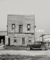 September 1937. "Boardinghouse in Littlefork, Minnesota." Medium format negative by Russell Lee for the Farm Security Administration. View full size.
Watch that first stepThe upper door, an old balcony/upper porch judging from the scars on the wall framing, reminds me that most buildings in the Colorado Rockies needed a way out when the snow was real deep. I wonder if this upper door was used the same way in winter.
Miss VickyThat 1932 Ford Victoria would be worth a small fortune, today
RadioThe lower right window pulls in an antenna wire and a ground wire outside the window framing.  I can't tell if the wire continues from the first roof post to the second.
3rd and FrontBoarding house was likely at 3rd and Front St, assuming this building is the larger one in the background (but viewed from another direction).

Got That Right Horace!1932 Ford V8 Victoria Average asking price $57,431; lowest price in last three years $26,500!
(The Gallery, Cars, Trucks, Buses, Russell Lee, Small Towns)