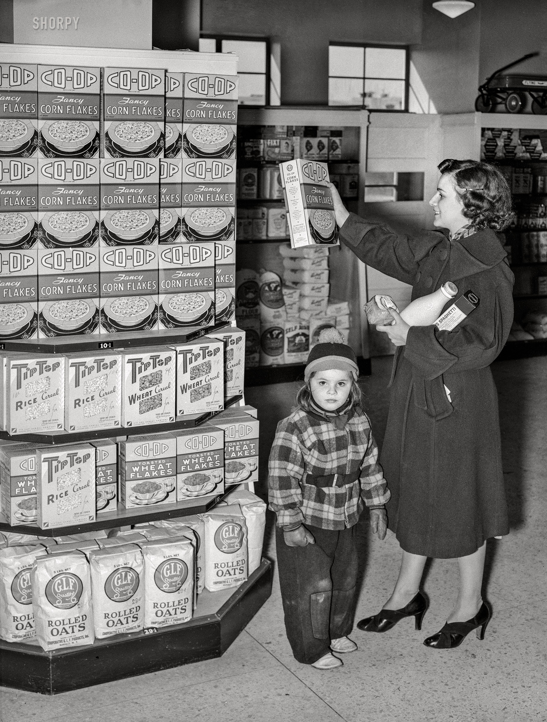 February 1938. "Resident at Greenbelt, Maryland, with child in the cooperative grocery store. Greenbelt is a model community planned by the Suburban Division of U.S. Resettlement Administration." Medium format acetate negative by Russell Lee. View full size.