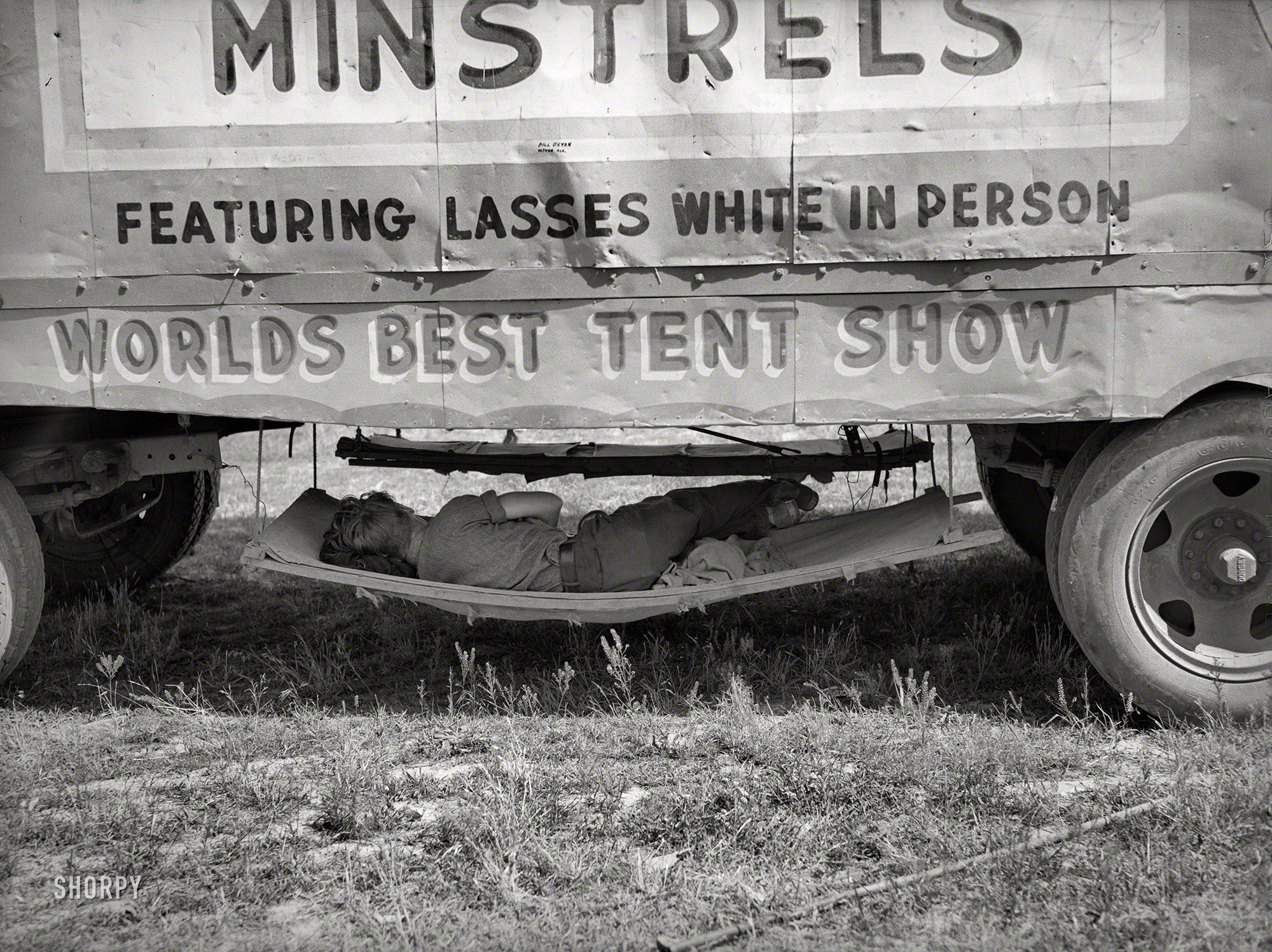 May 1938. "Carnival employee sleeping in hammock underneath wagon of Lasses White show. Sikeston, Missouri." Photo by Russell Lee. View full size.