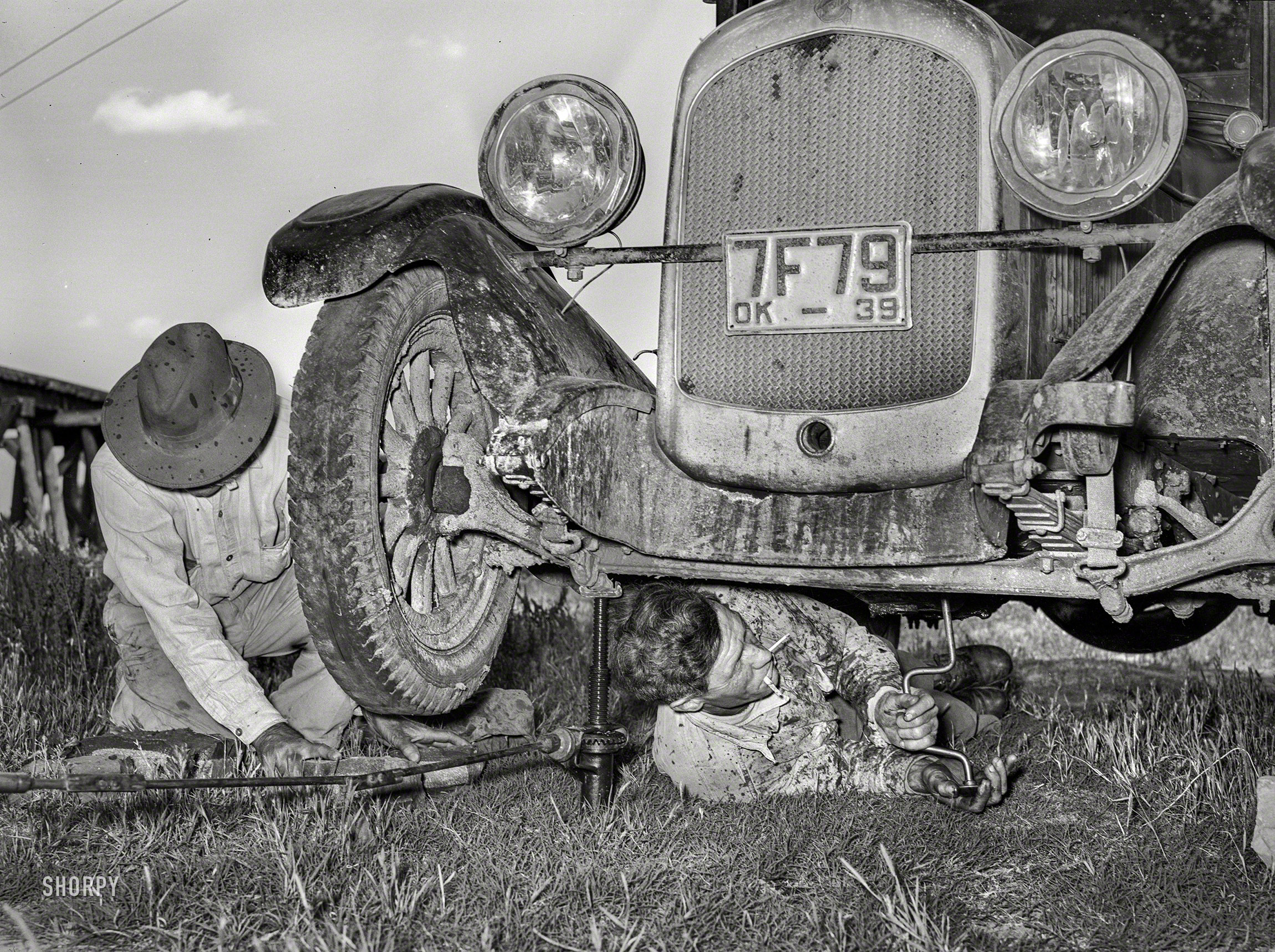 June 1939. "Migrant steeplejack removing the crankcase from his automobile while his father blocks up the front wheel near Prague, Oklahoma. When he secures a job, the entire family, consisting of his father and mother, wife and sister, all help with the painting." Acetate negative by Russell Lee. View full size.