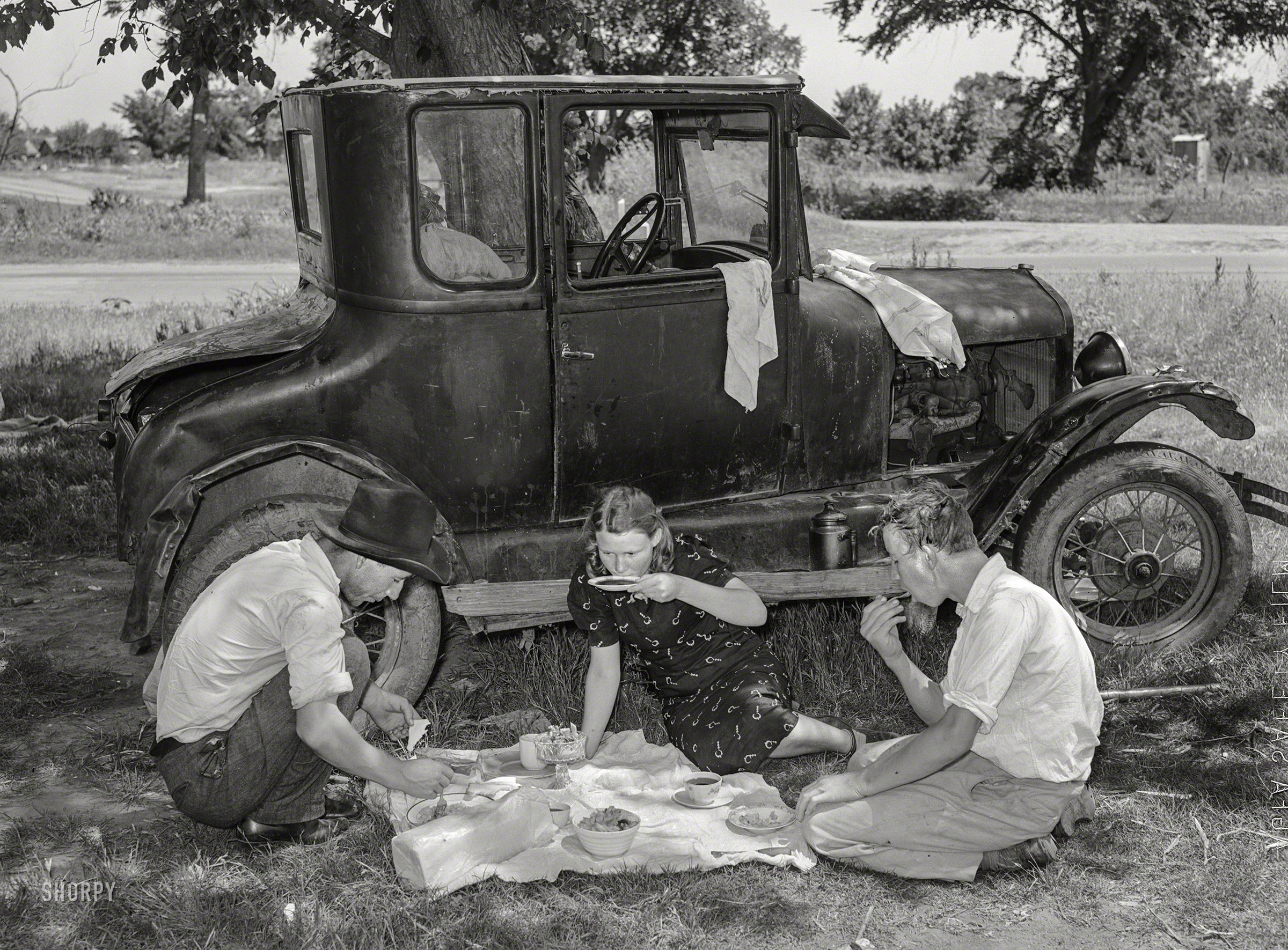 June 1939. "Migrant workers eating dinner by the side of their car (Ford Model T) while they are camped near Prague, Lincoln County, Oklahoma." Medium format negative by Russell Lee for the Farm Security Administration. View full size.