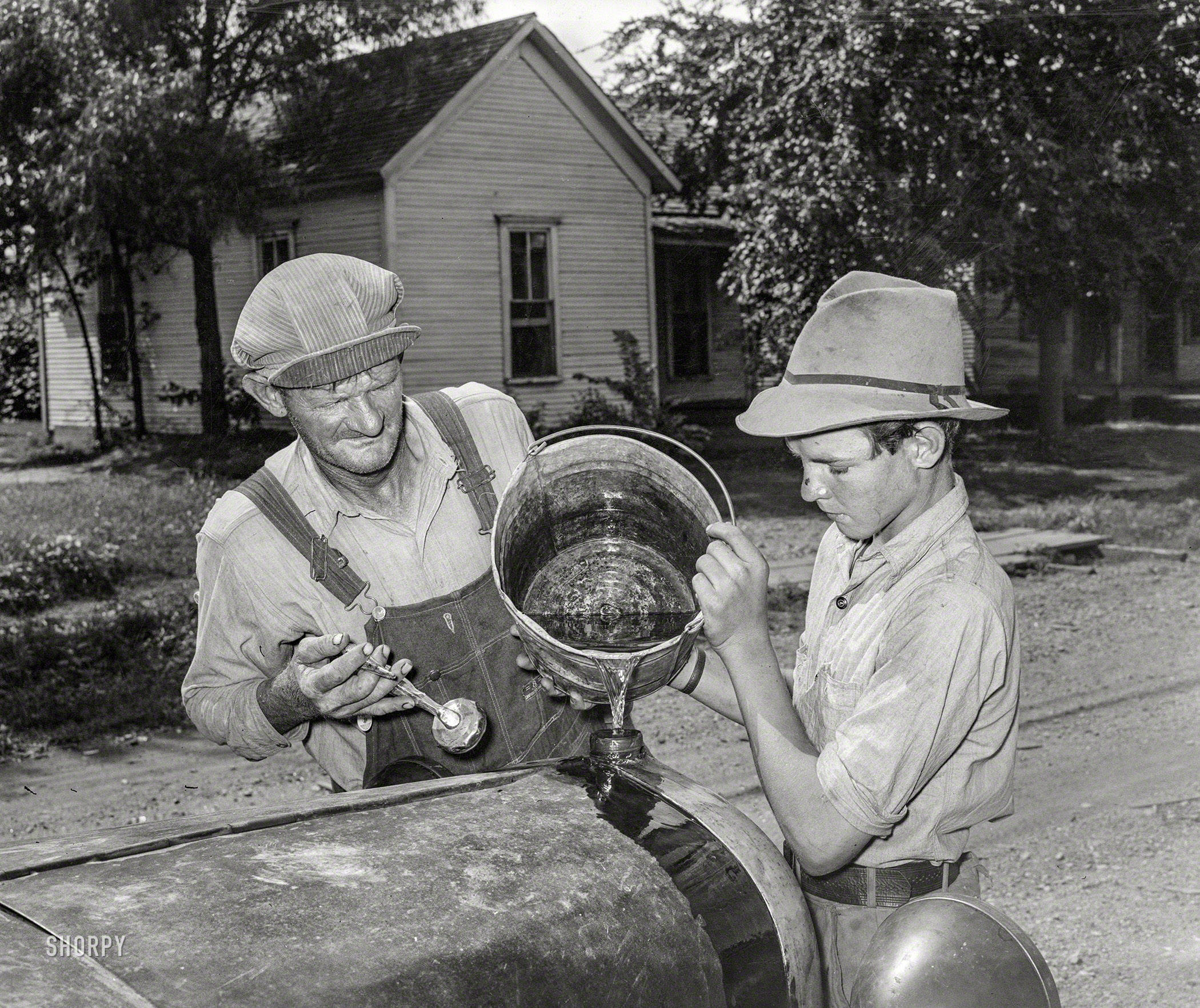 July 1939. "En route to California. Pouring water into radiator of migrants' car in the streets of Muskogee, Oklahoma, where the Elmer Thomas family has stopped to say goodbye to their friends in that town." Medium format acetate negative by Russell Lee for the Farm Security Administration. View full size.
